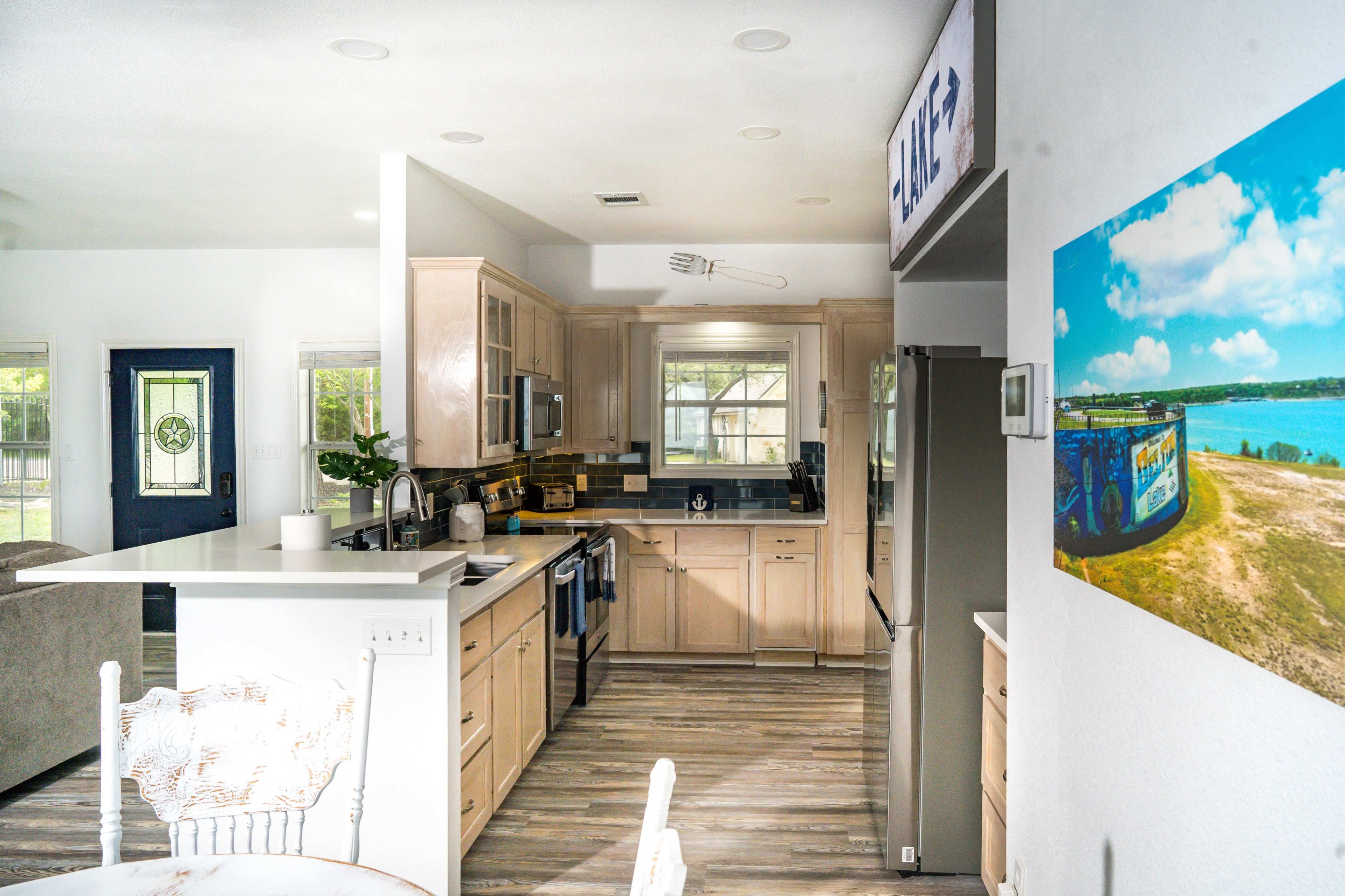 A modern kitchen features light wood cabinetry, stainless steel appliances, and an open layout with a dining area.