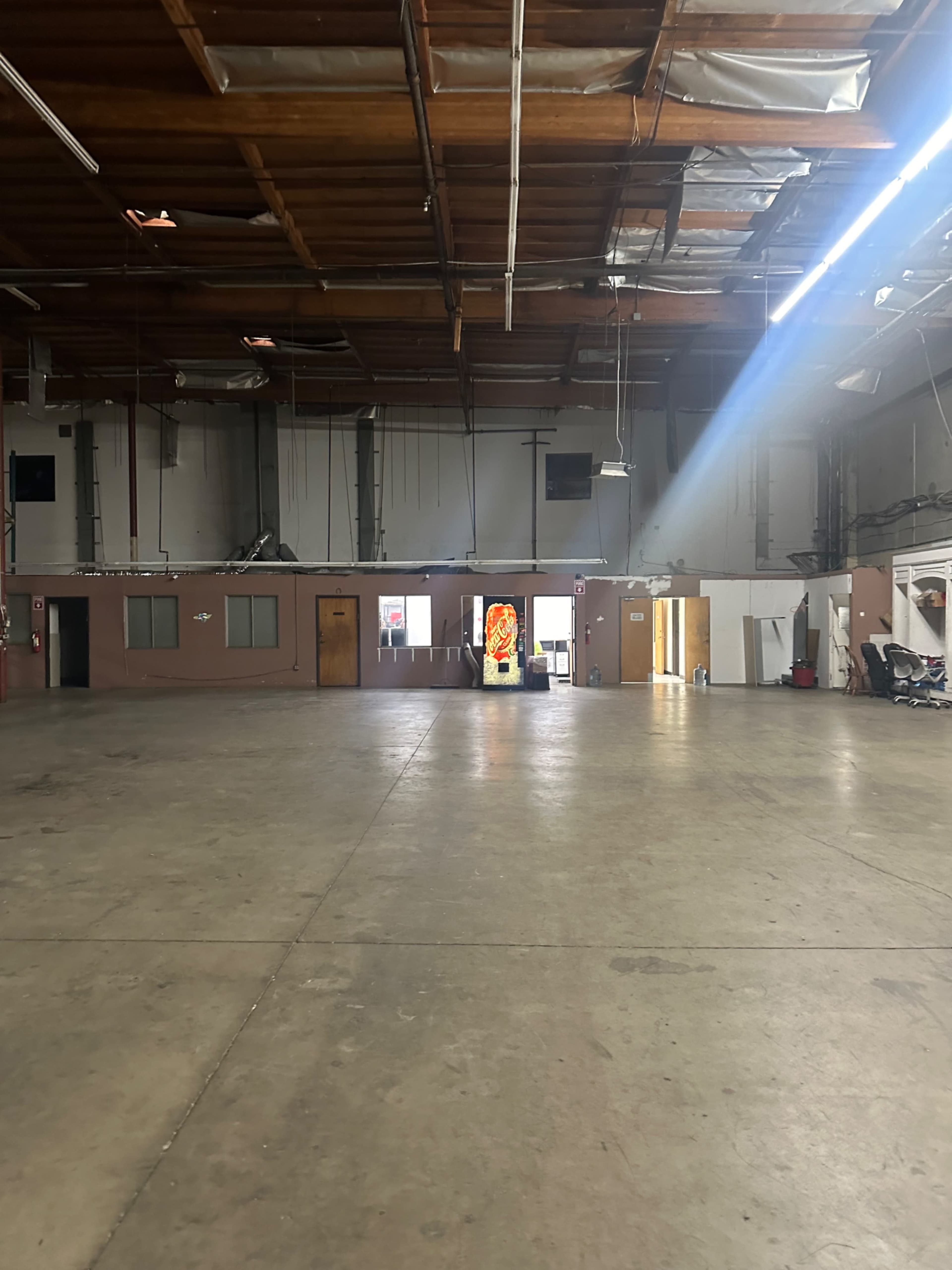 The image shows an empty warehouse space with concrete flooring and a faint light shining towards an open doorway.
