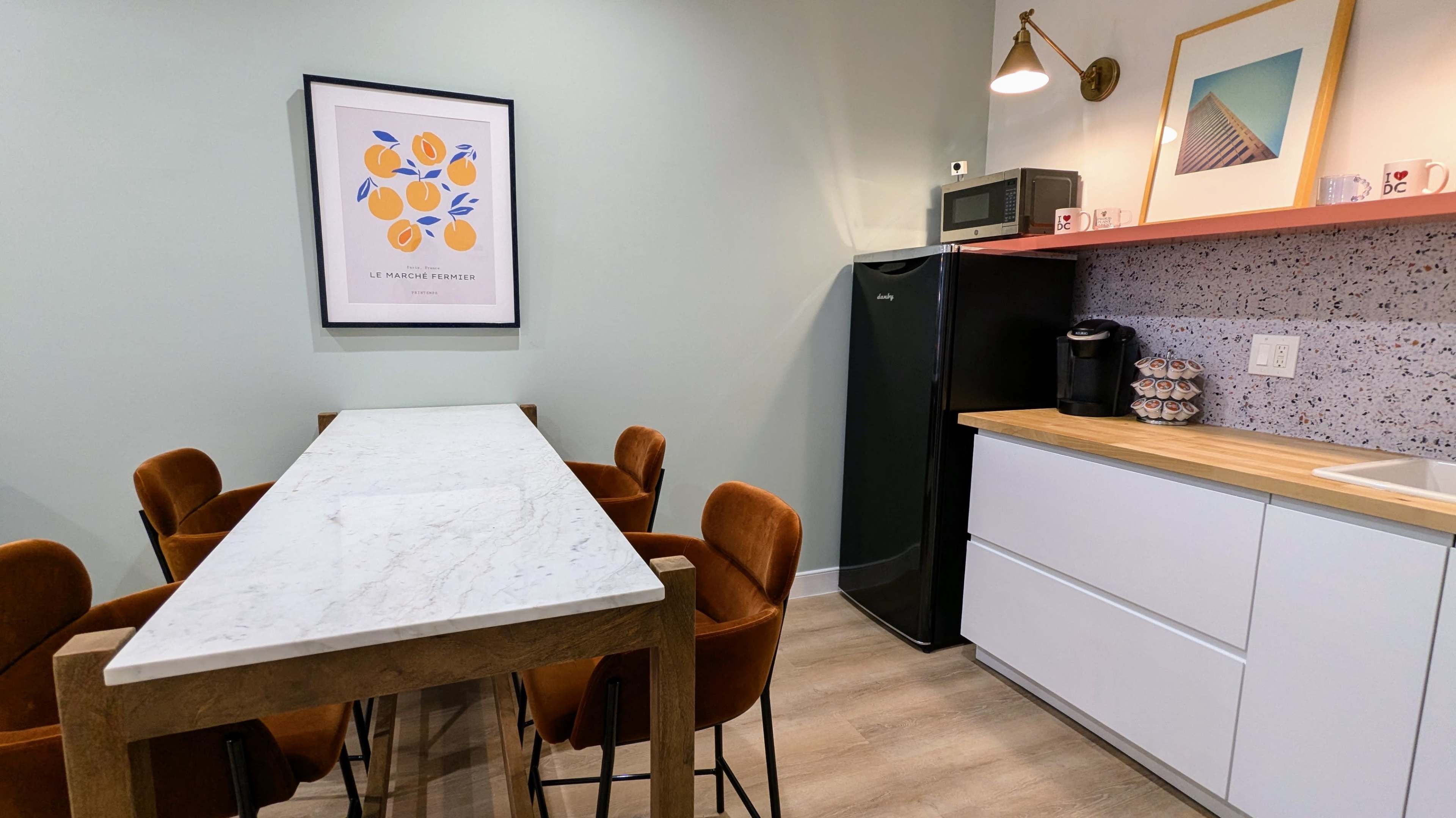 A modern kitchen with a marble table and brown chairs, a black refrigerator, a microwave, and a countertop with a coffee maker and decorative items.