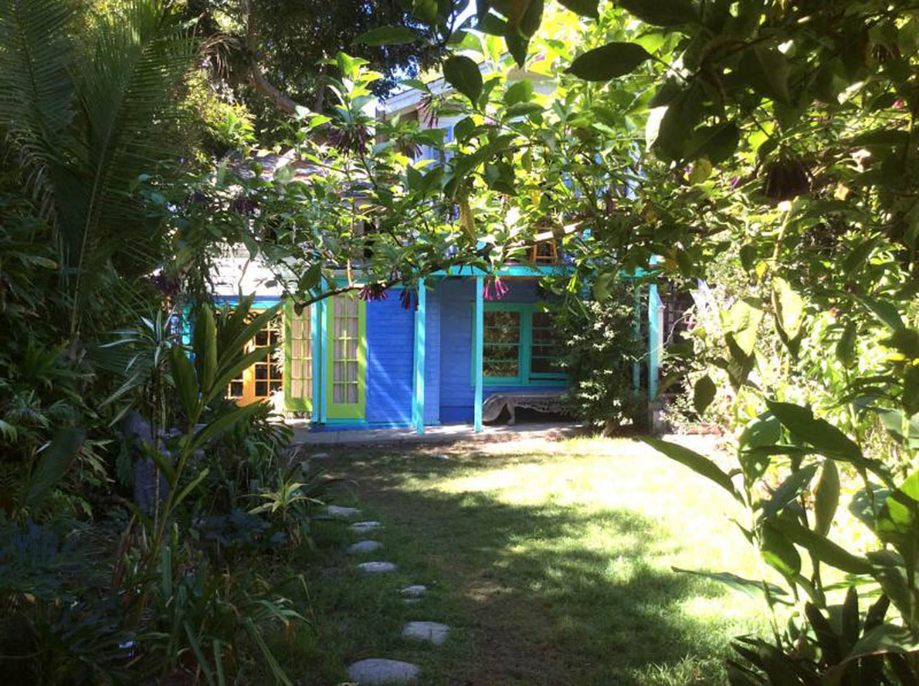 A colorful house with blue and yellow elements is surrounded by lush greenery in a garden setting.