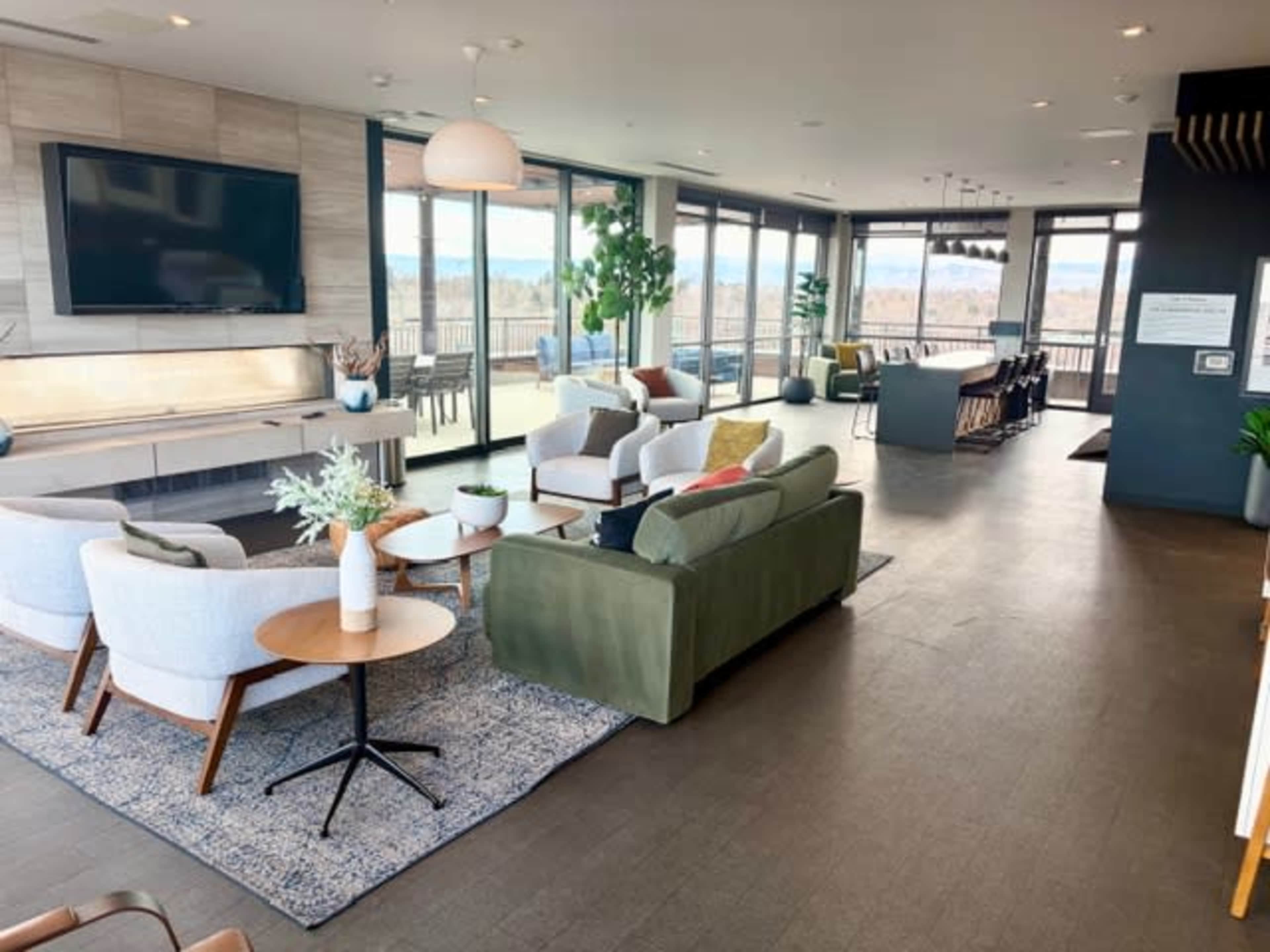 The image shows a modern, open-concept living area with large windows, comfortable seating, and a view of the outdoors.