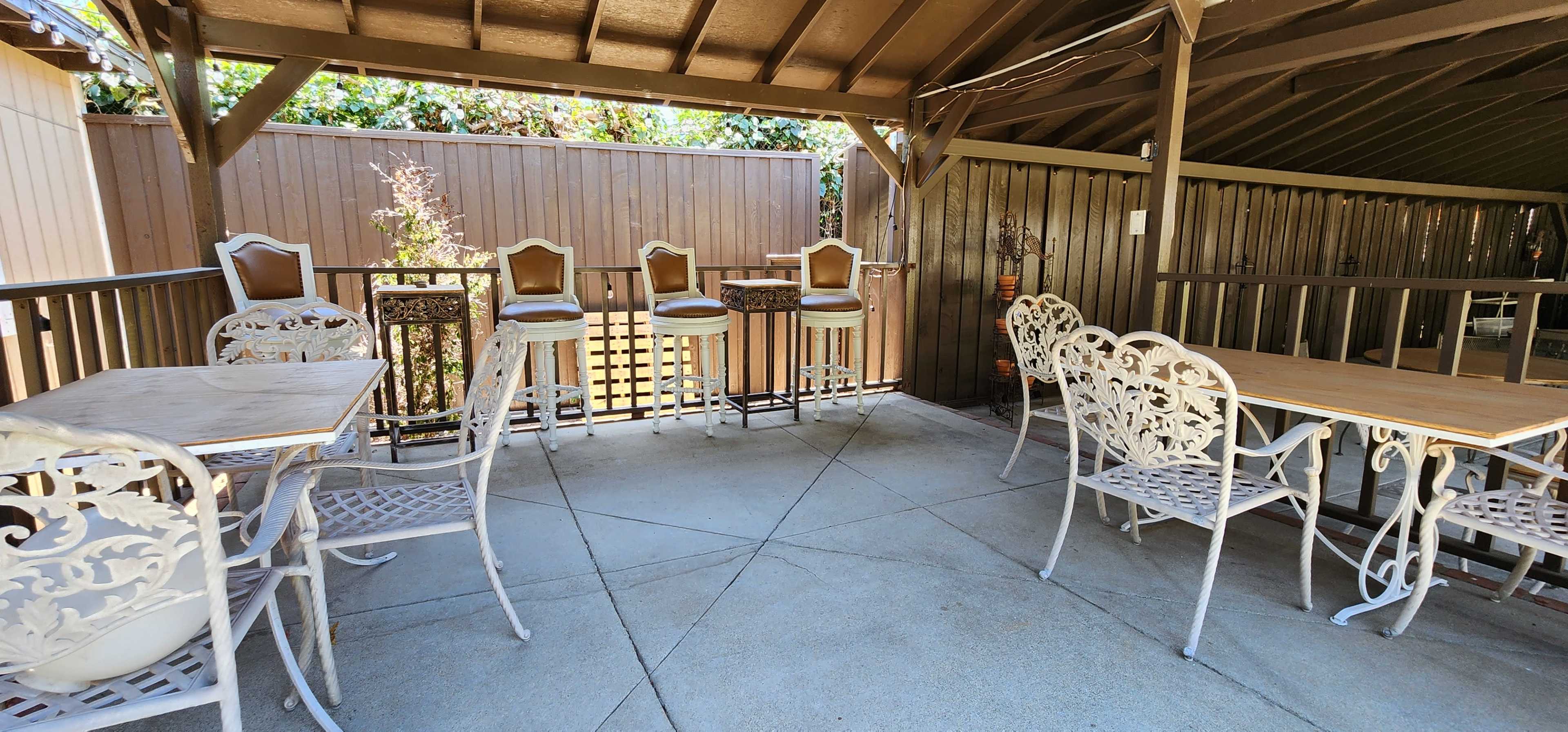 An outdoor patio with several wrought iron tables and chairs, along with bar stools positioned at a ledge.