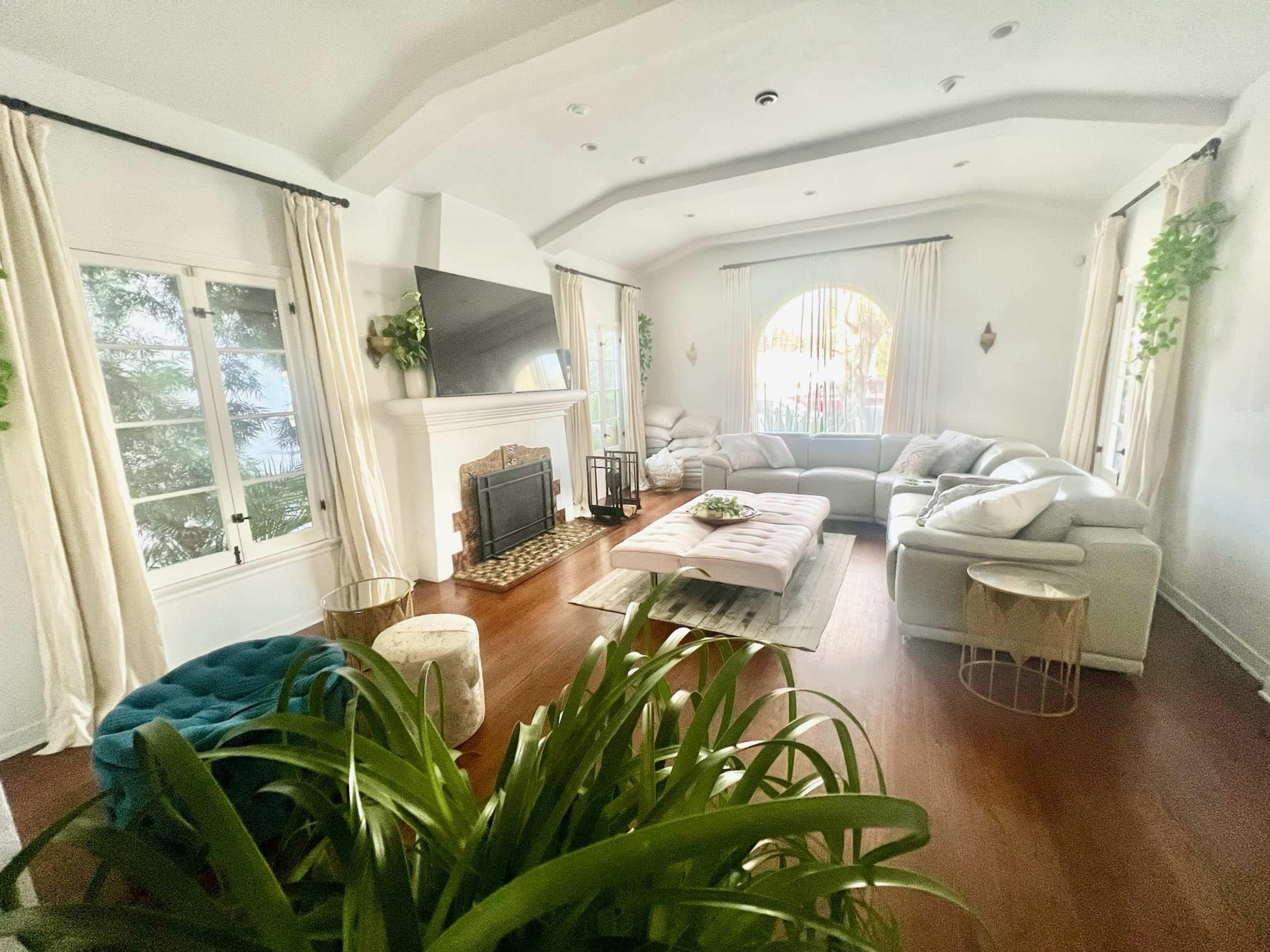 The living room features a white sectional sofa, a large coffee table, and a fireplace, with large windows allowing natural light to flow in.