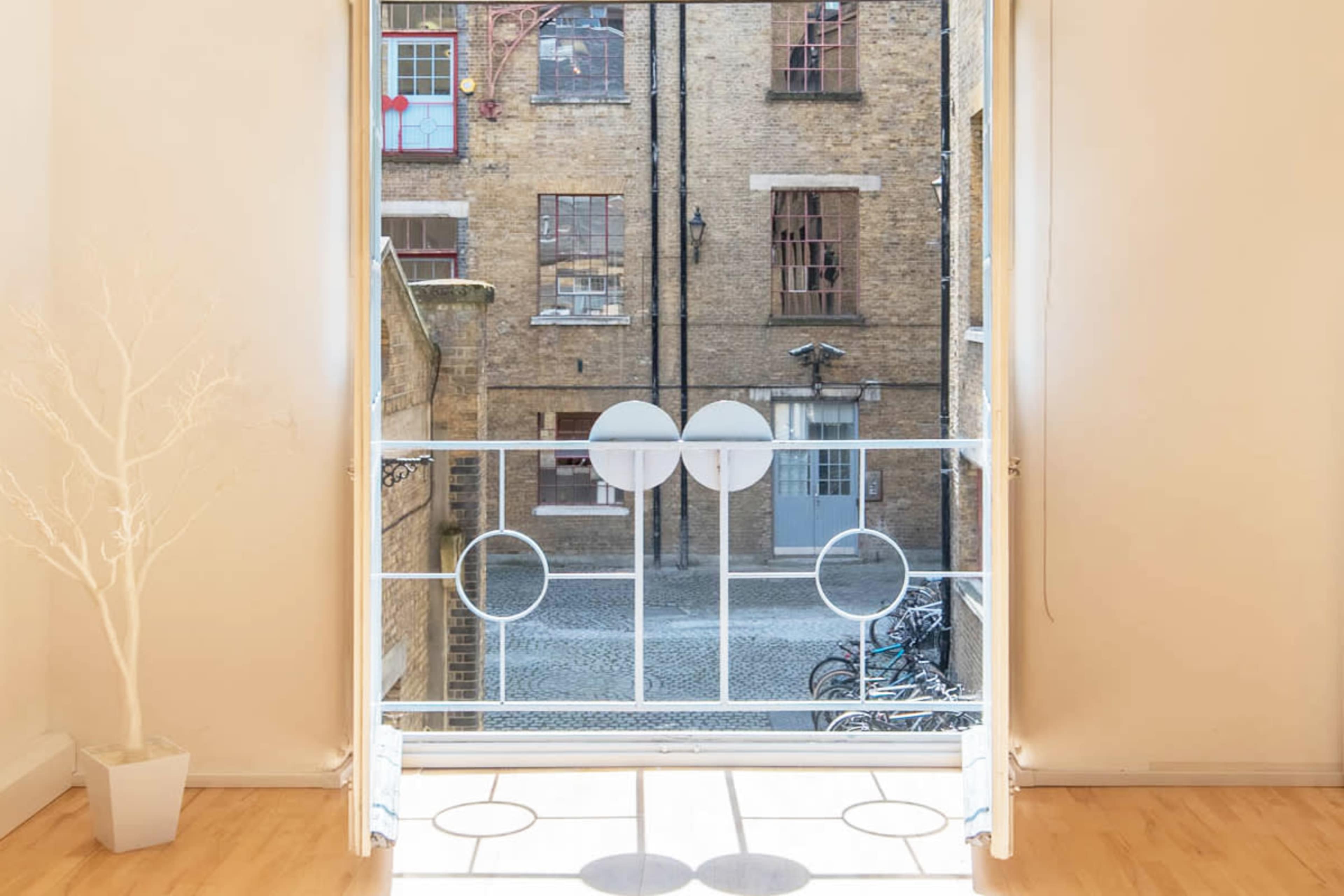 A white balcony railing frames a view of a cobblestone courtyard with bicycles parked against the wall of a brick building.