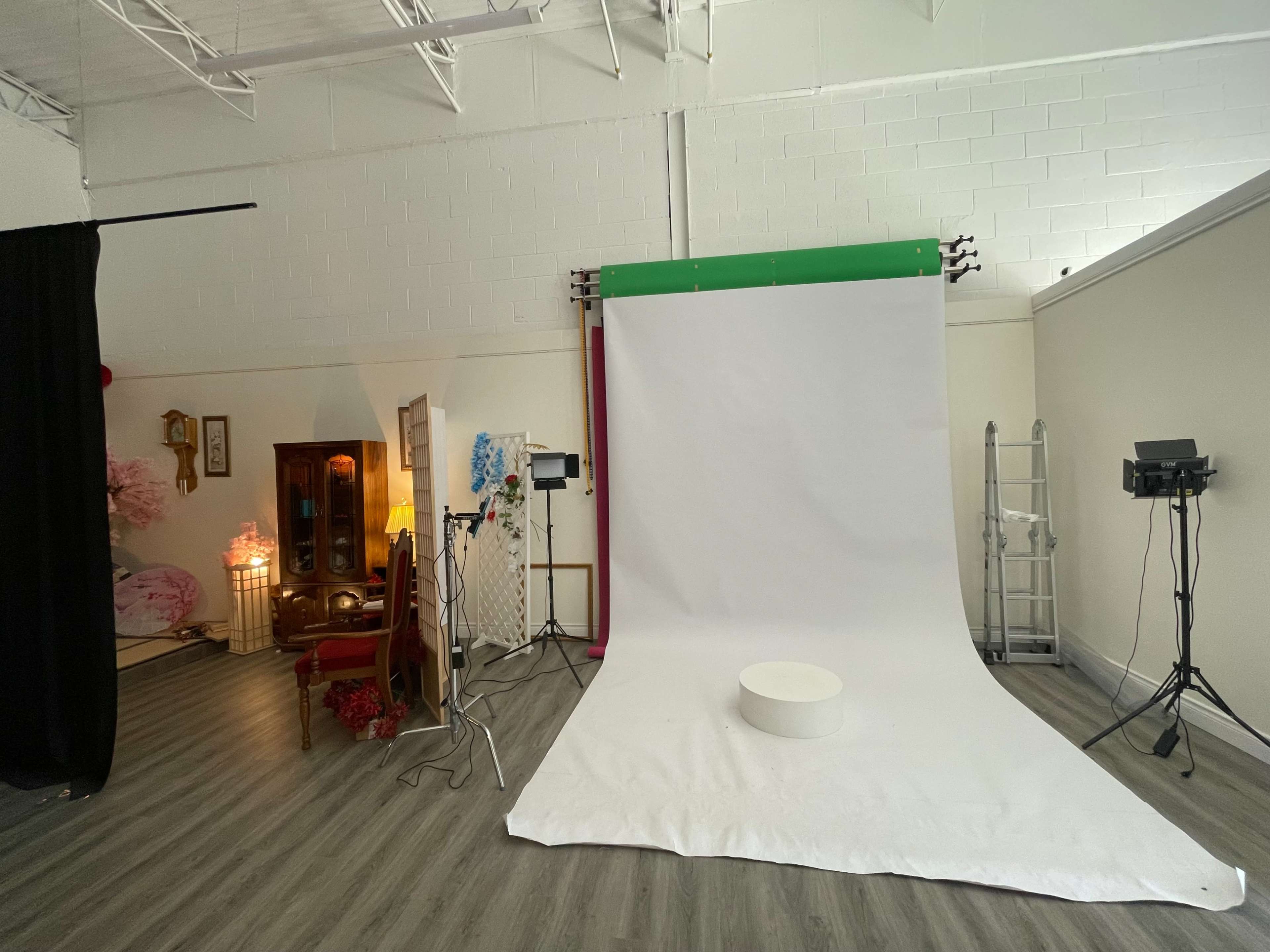 The image shows a photography studio with a white backdrop, various lighting equipment, and a decorative chair set against the walls.