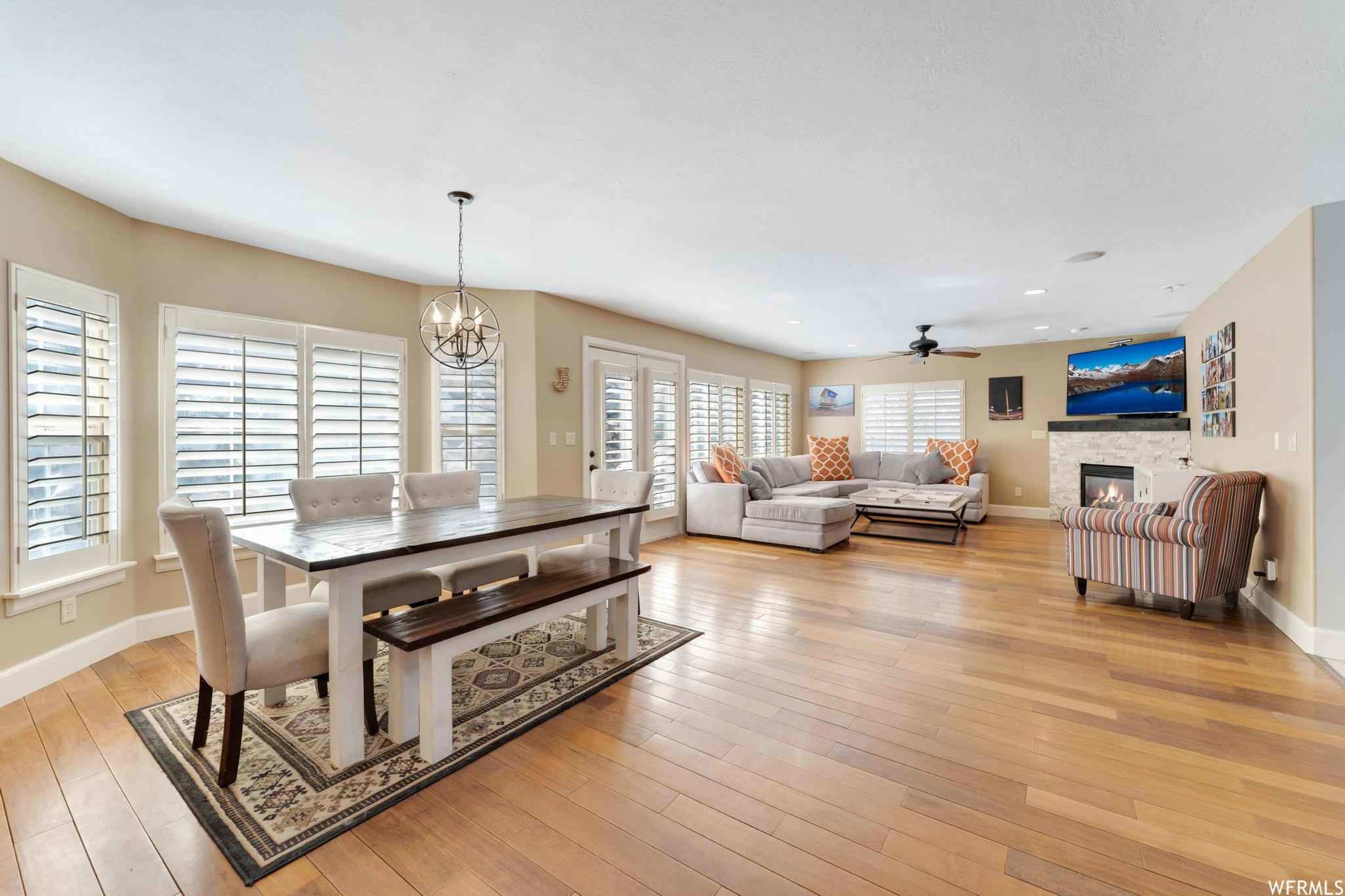 The spacious living and dining area features a large table, comfortable seating, and multiple windows with plantation shutters.