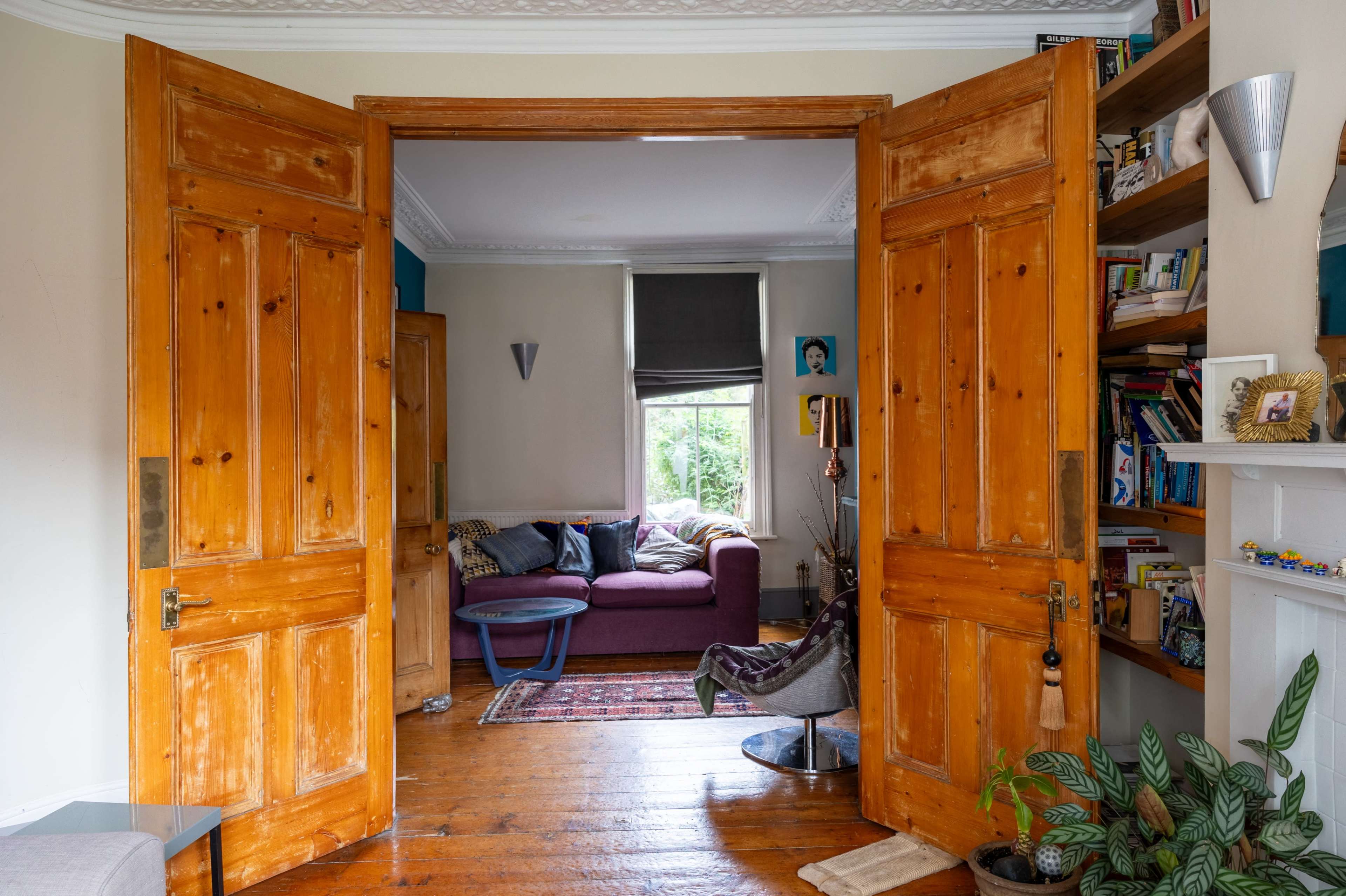 A pair of open wooden doors leads into a bright living room featuring a purple couch and a small table.
