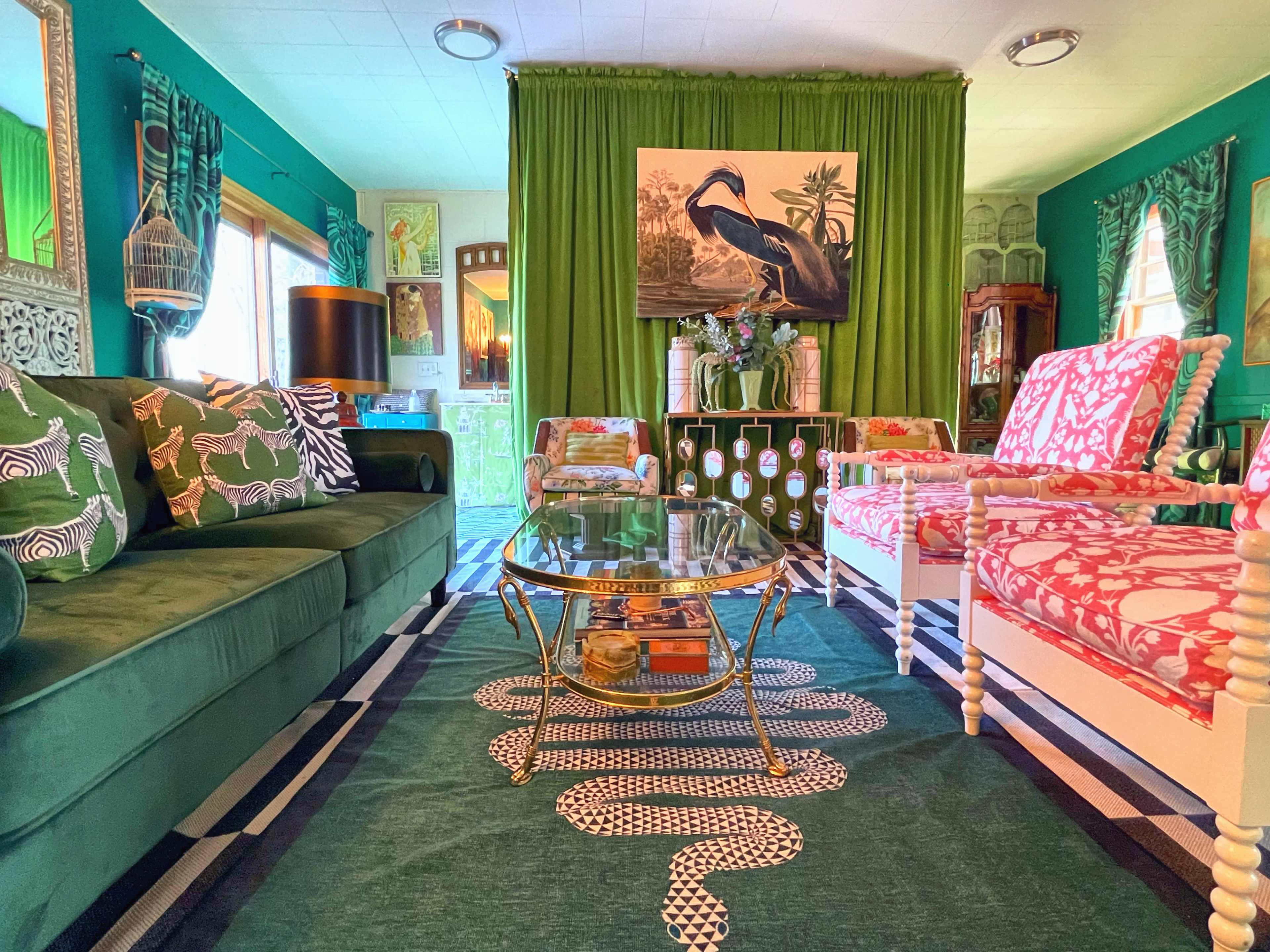 The living room features a green color scheme with a variety of patterned furniture, a glass coffee table, and a large painting of a bird on the wall.