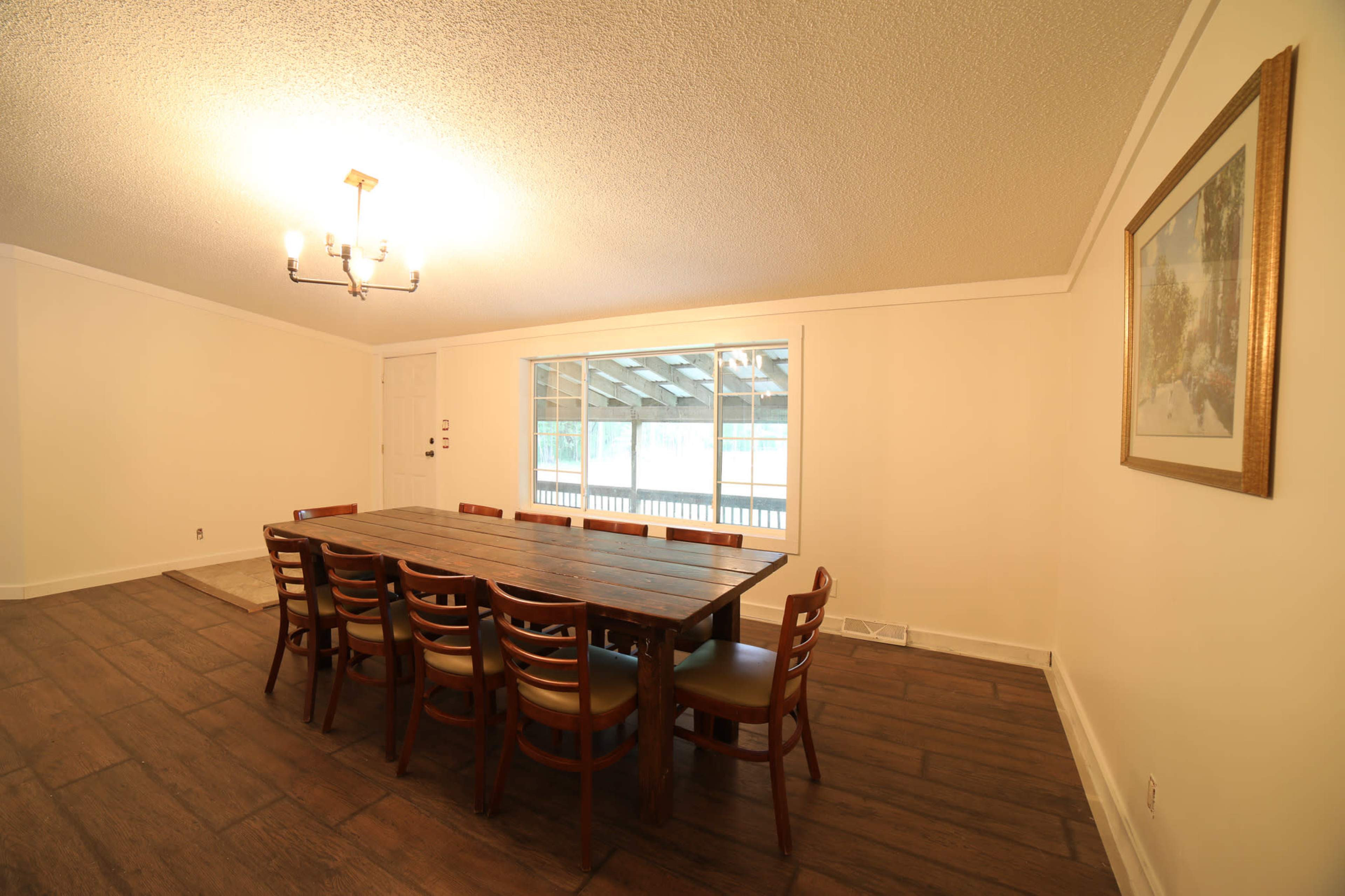 A spacious dining room features a long wooden table surrounded by chairs, with a large window offering a view of the outdoors.