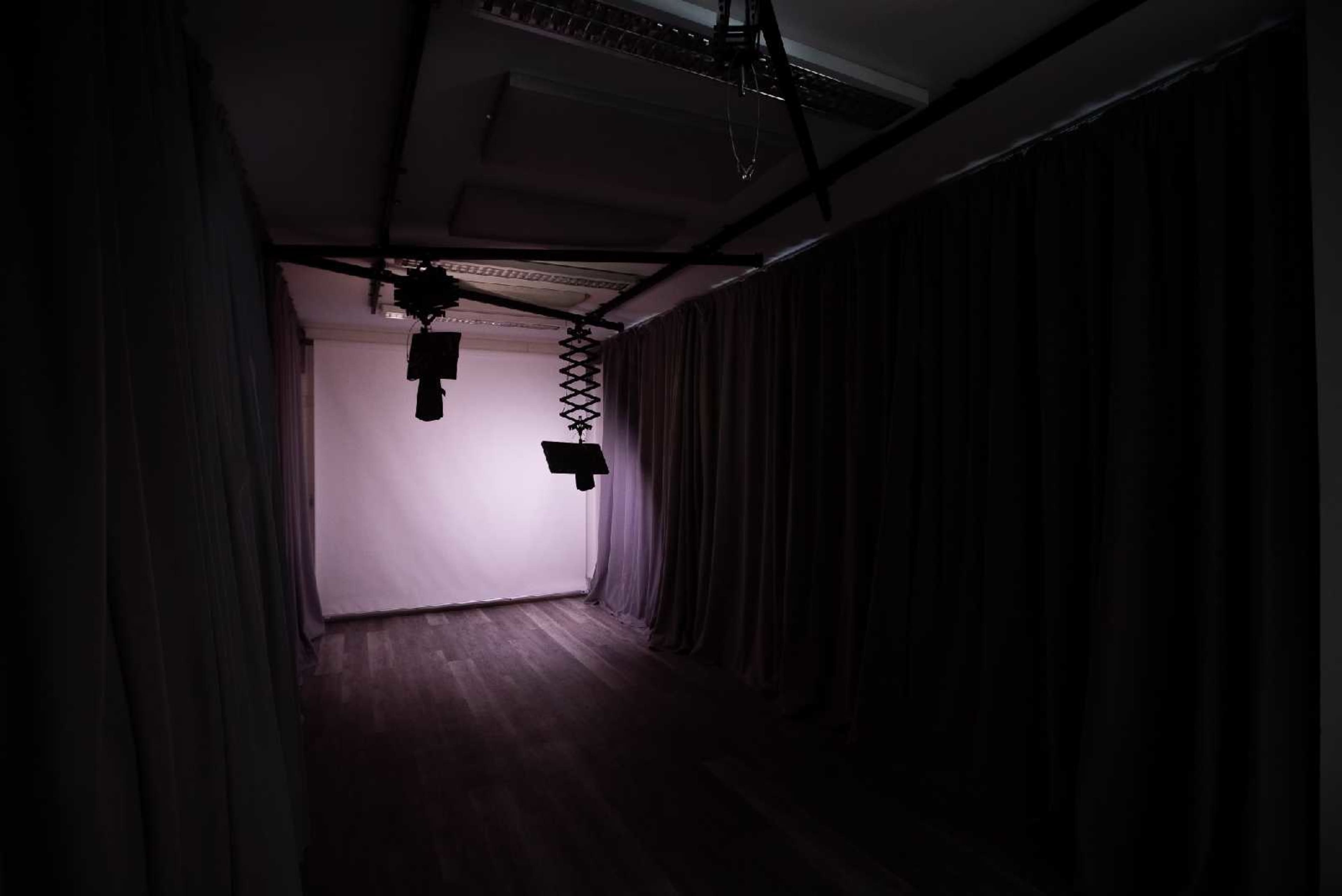 A dimly lit studio space with curtains lining the walls, featuring a light fixture and a movable backdrop in the center.