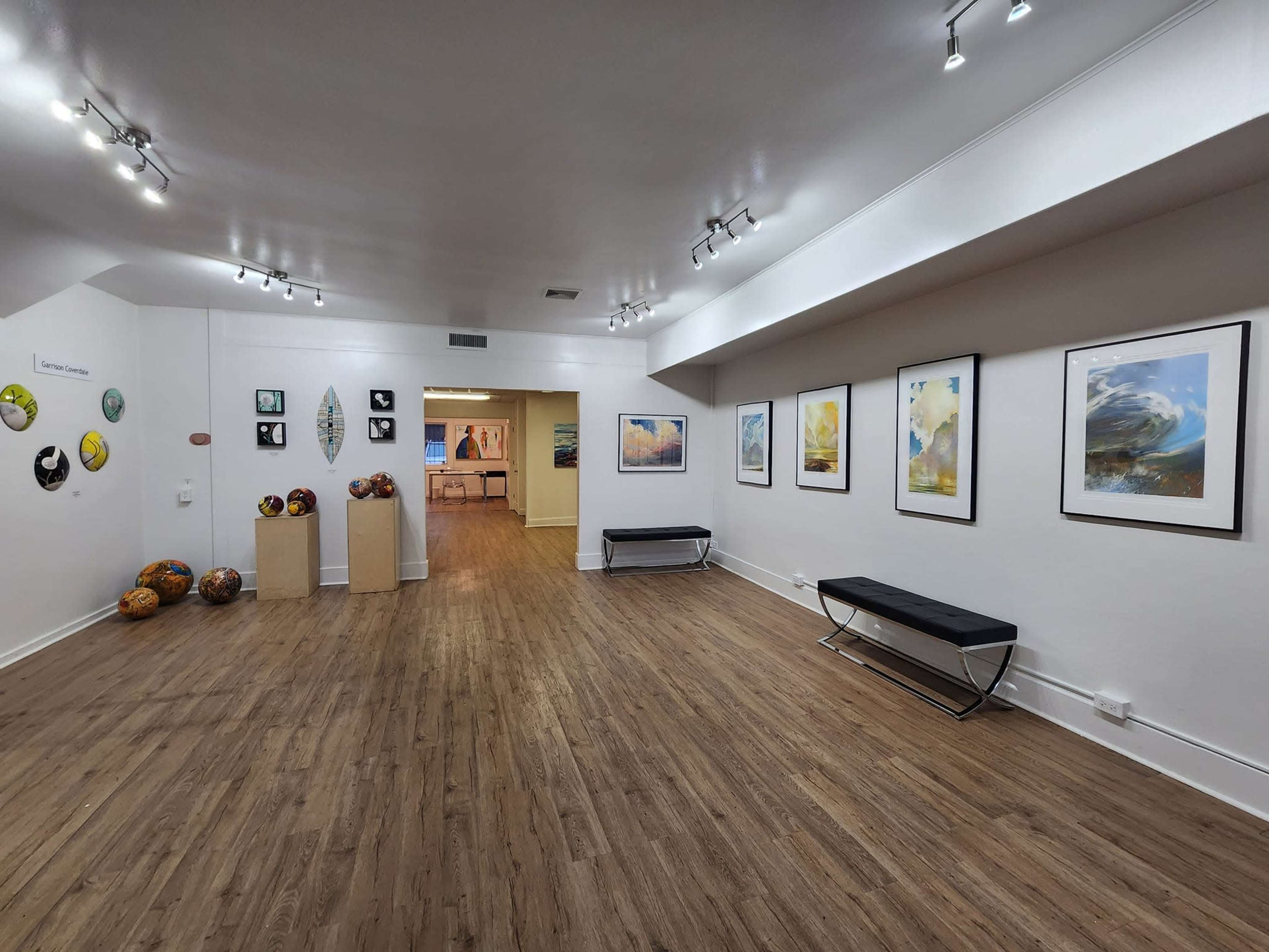 An art gallery featuring several paintings on white walls, a wooden floor, and a few sculptures displayed on pedestals.