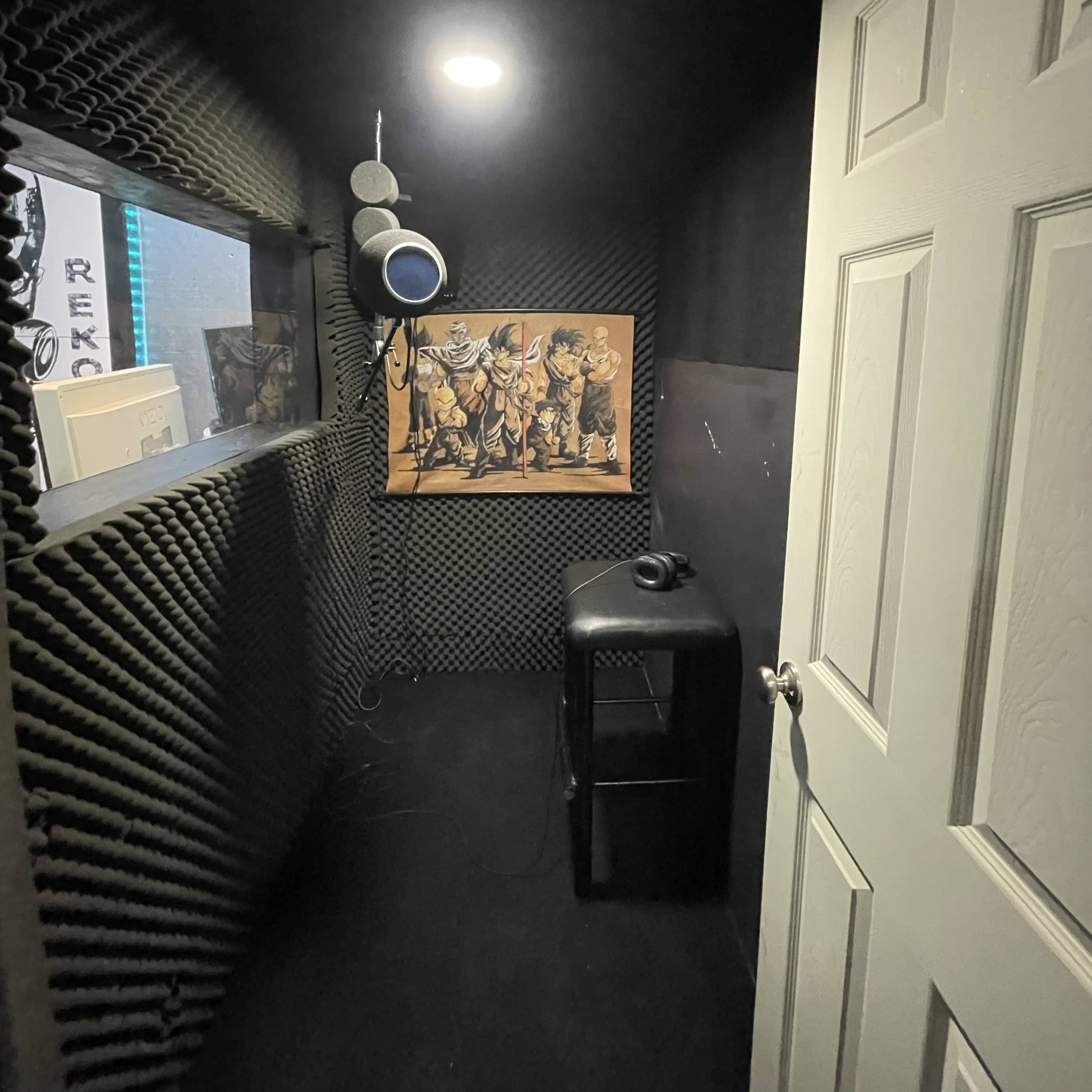 A soundproof room with acoustic foam walls, a door, a black cabinet, and a painting of figures on the wall.