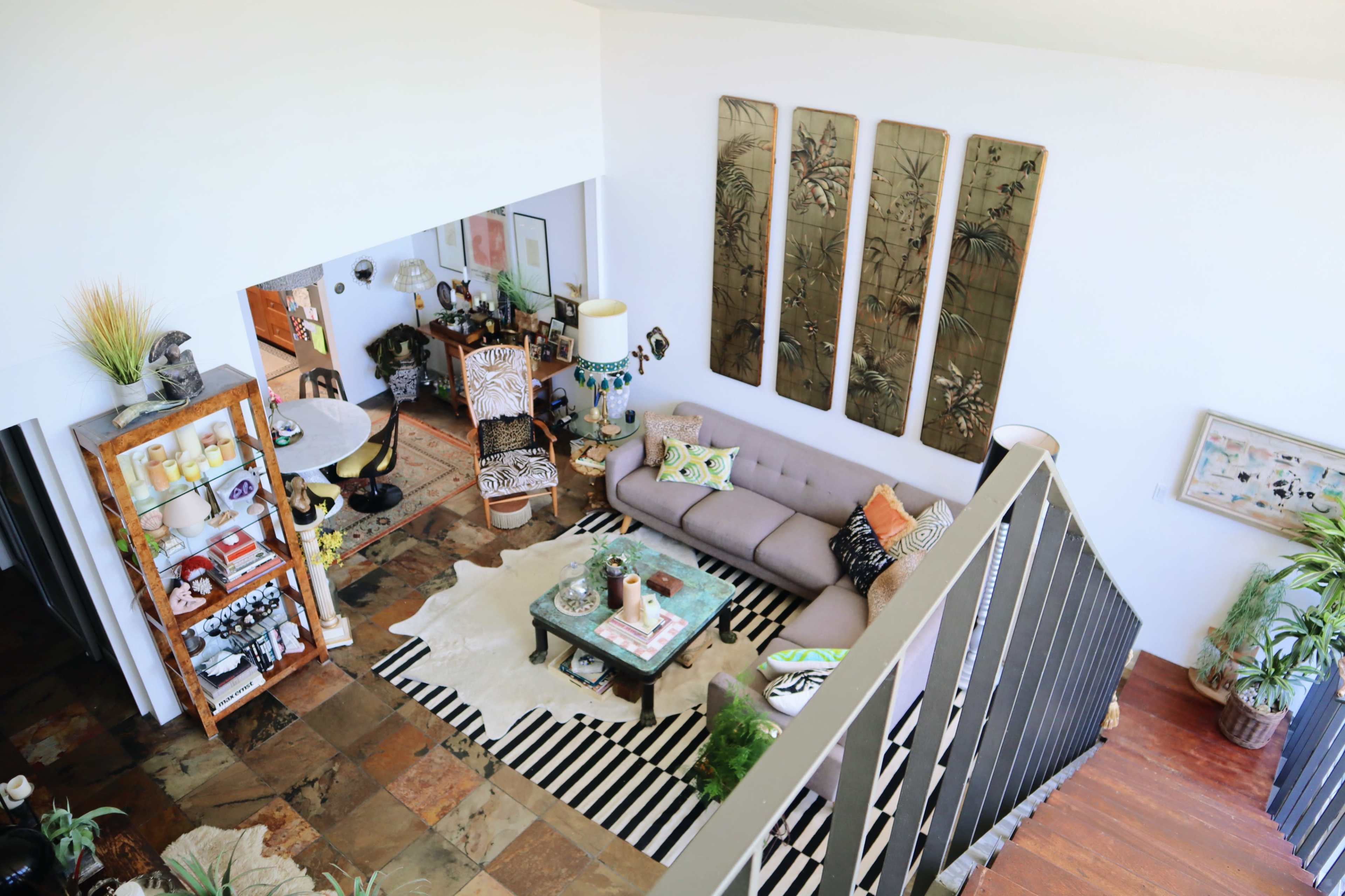 A spacious living room and dining area featuring a gray sofa, patterned area rugs, and decorative plants.