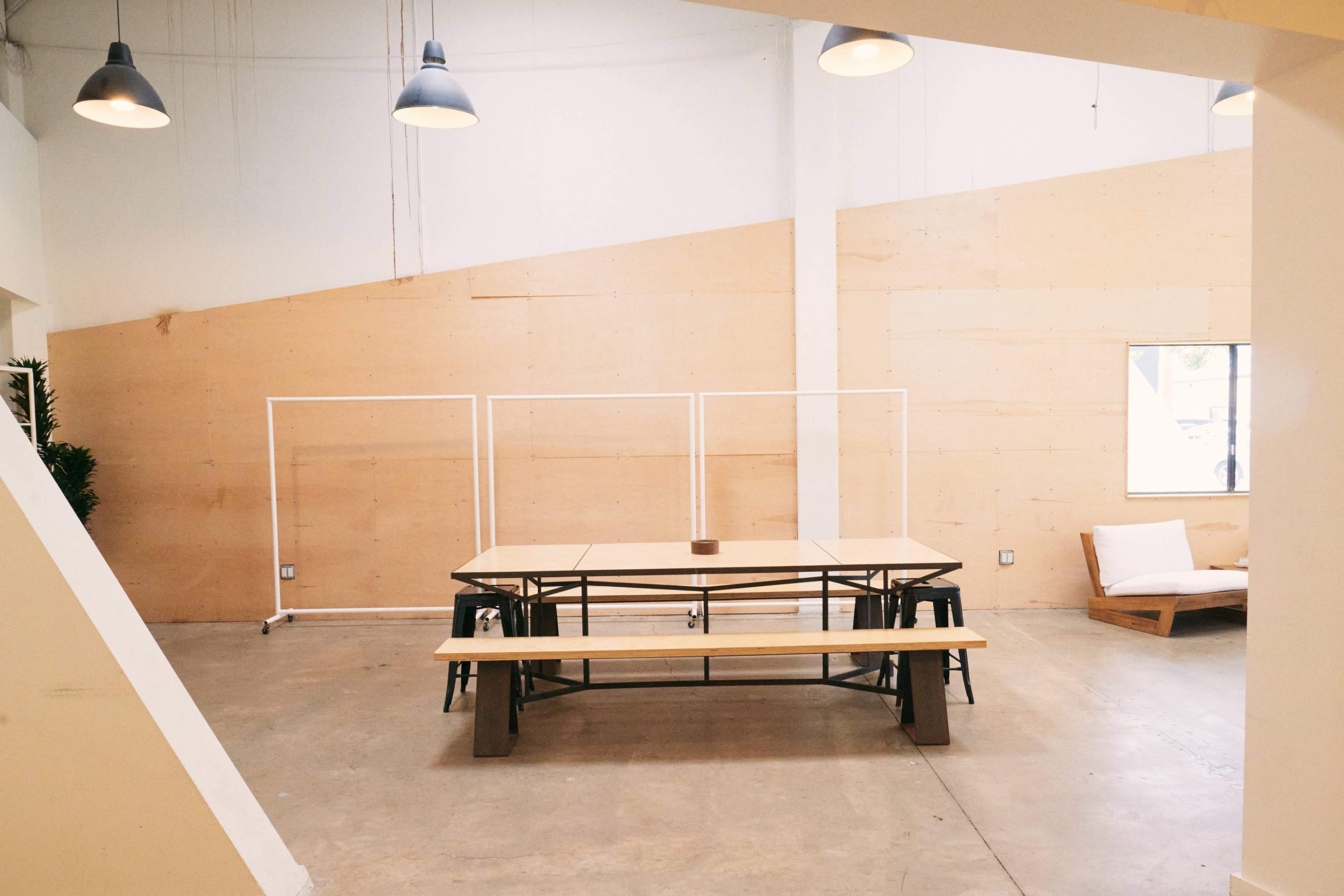 A spacious interior with a large wooden table and benches, surrounded by minimalist decor and a light-colored wall.