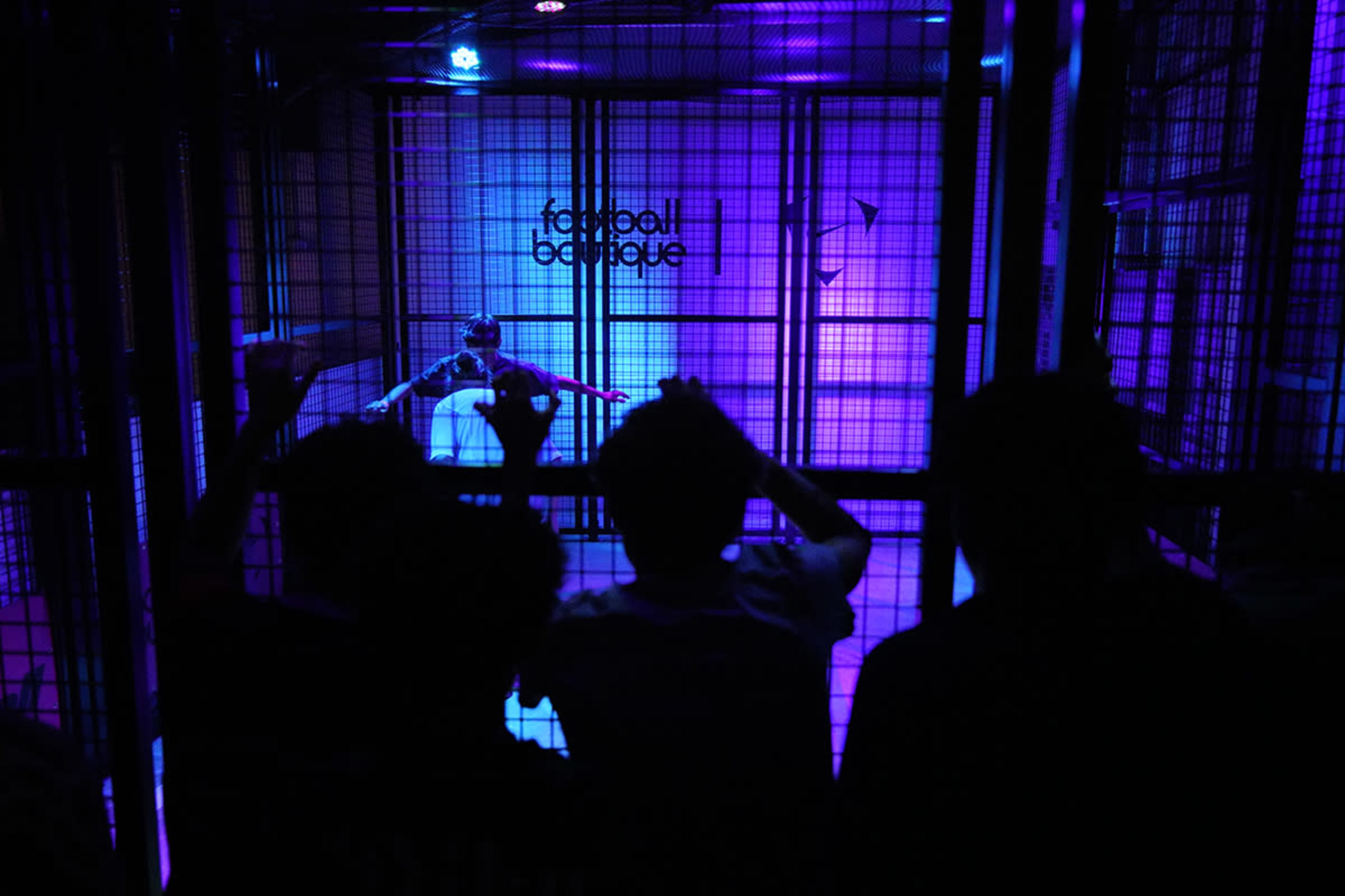 A group of people watches a performer inside a brightly lit, enclosed stage area.