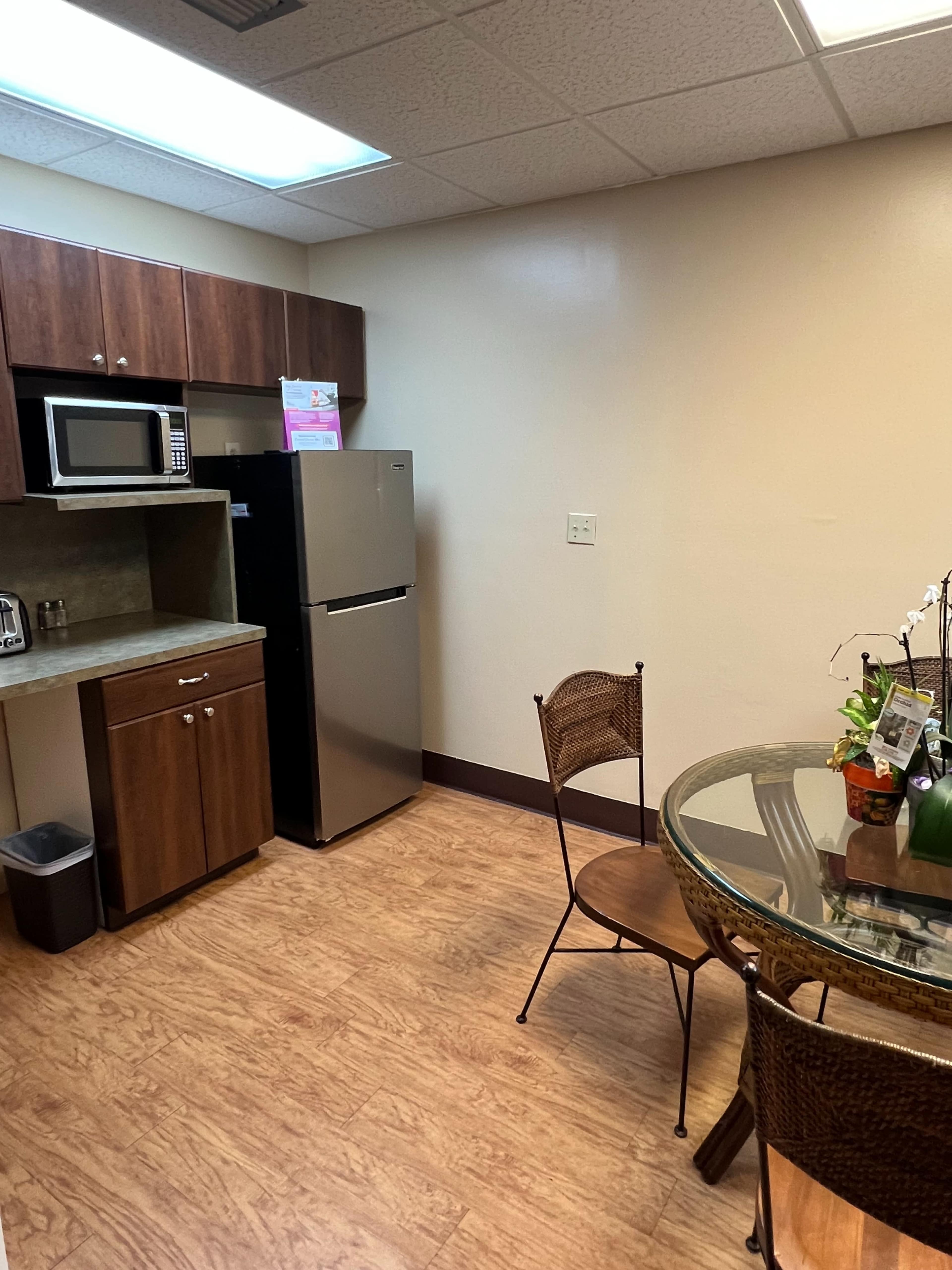 A kitchen space with wooden cabinets, stainless steel appliances, and a round glass dining table with metal chairs.