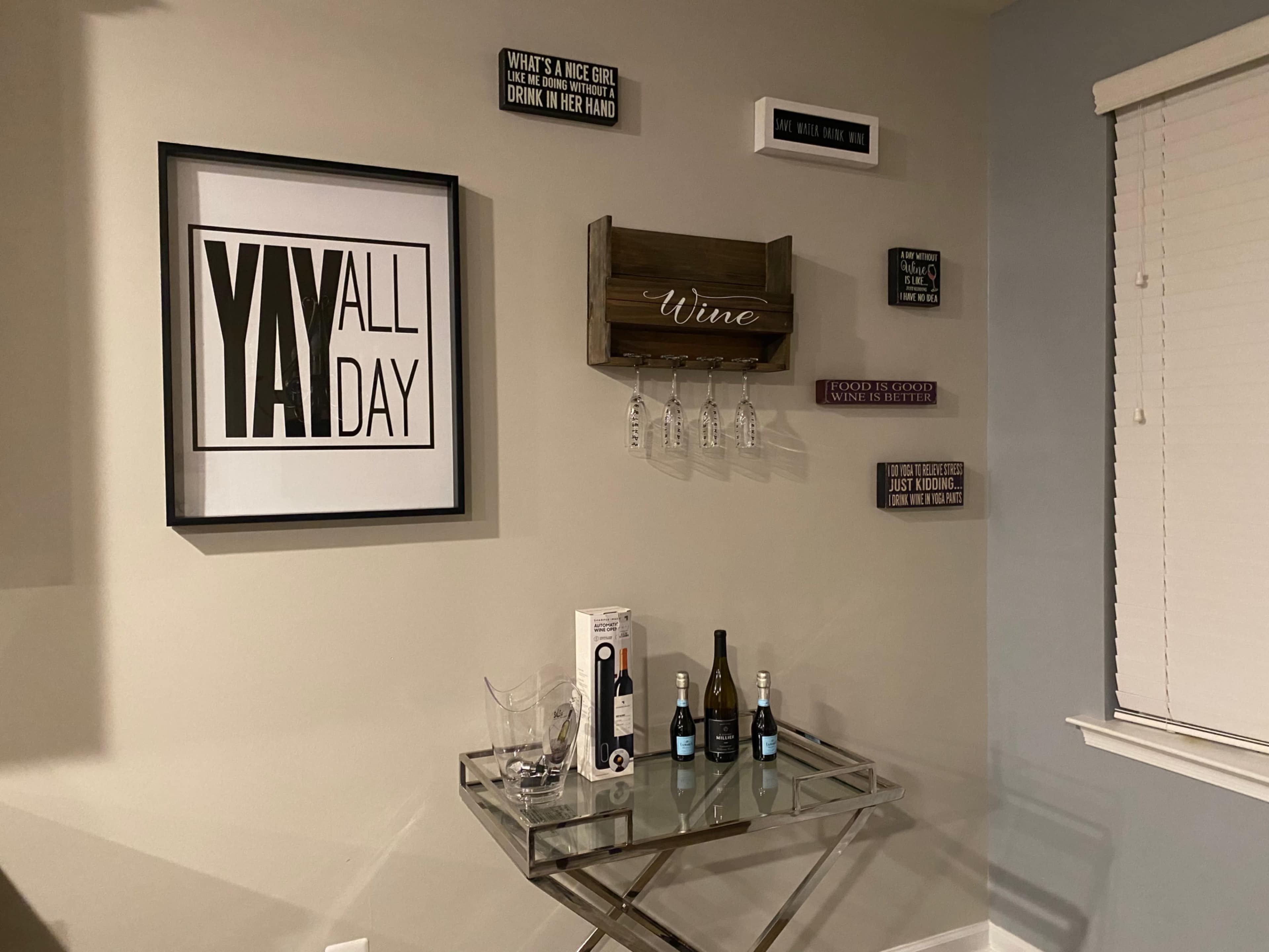 The image shows a decorative wall with various signs and a wine rack, alongside a glass table featuring wine bottles and glasses.