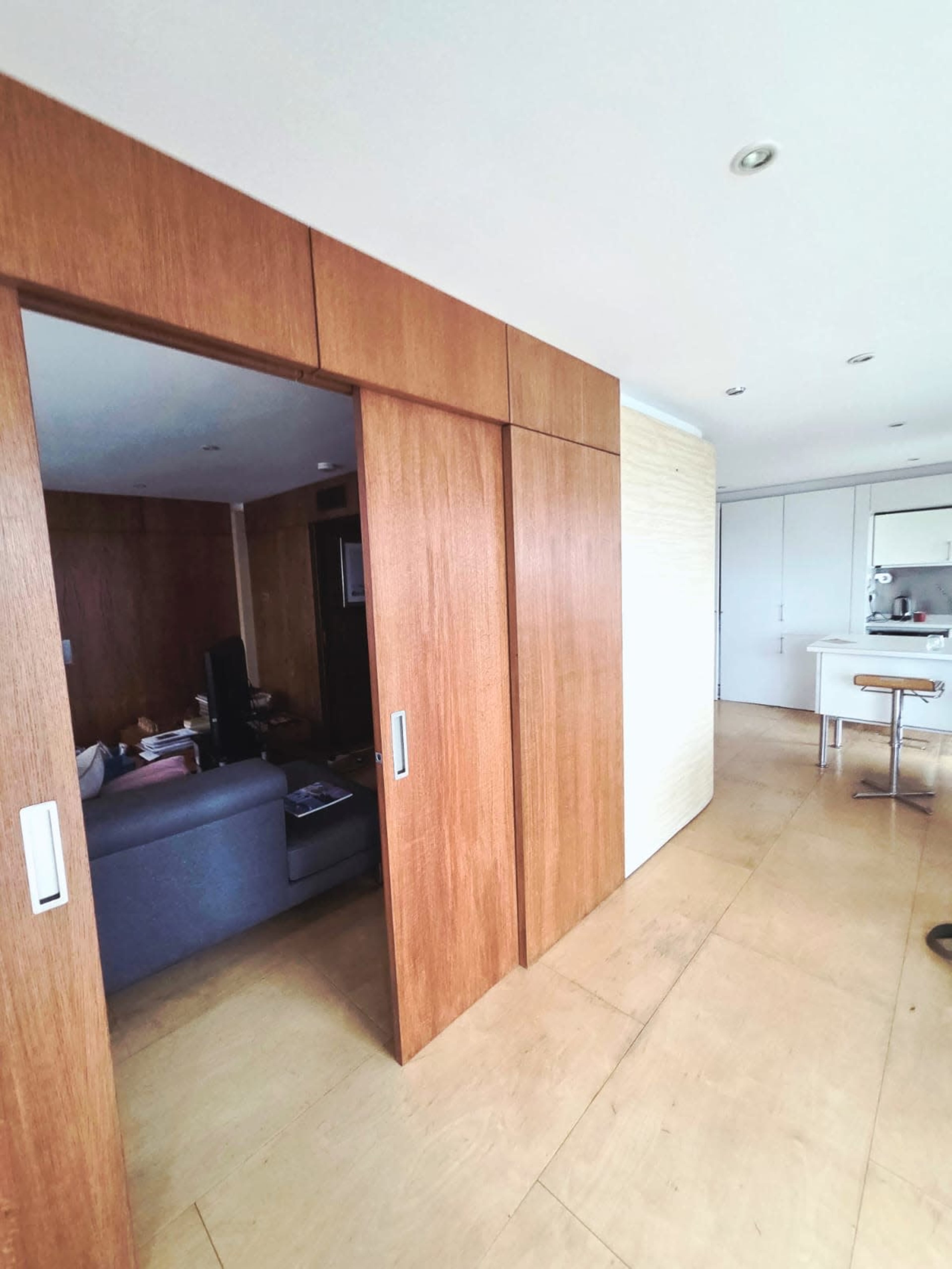 The image shows a hallway leading to a room with wooden sliding doors and a view of a kitchen area in the background.