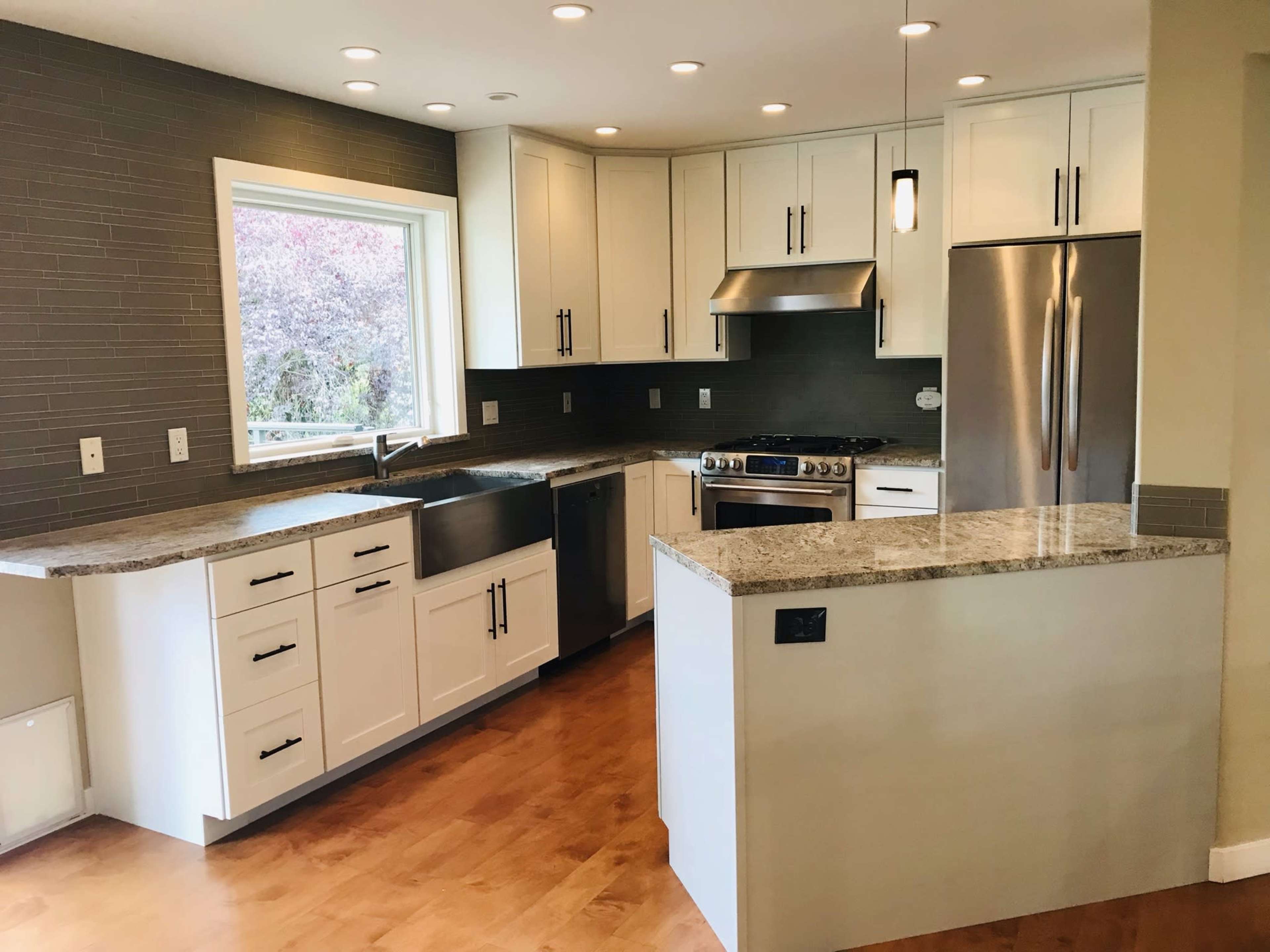 A modern kitchen with white cabinets, granite countertops, stainless steel appliances, and a large window above the sink.