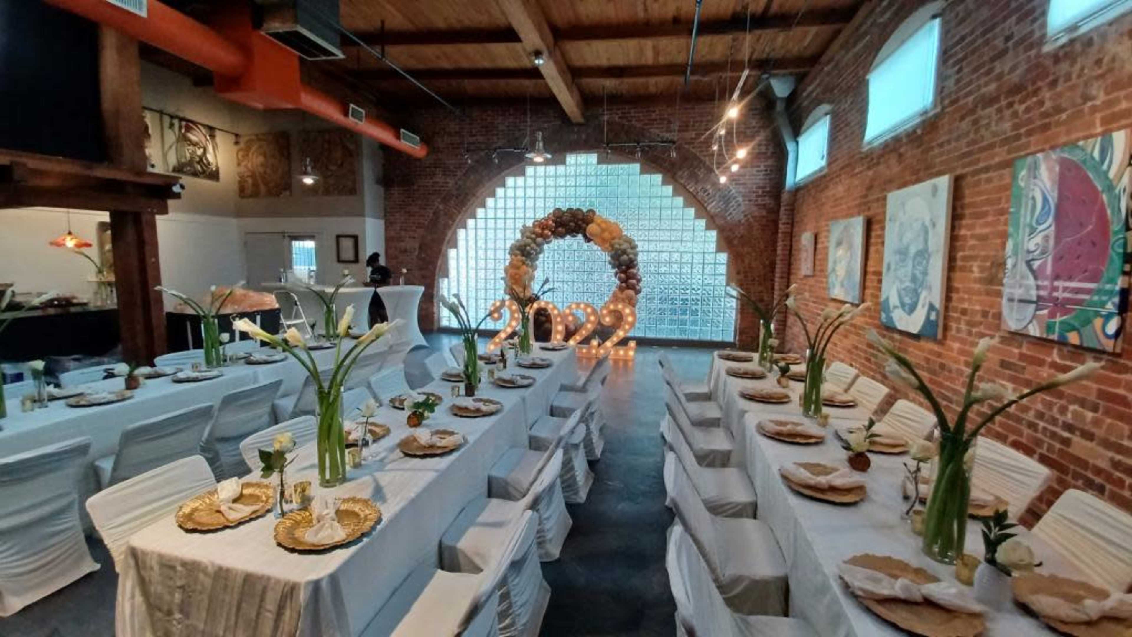 A banquet hall features long tables set for a celebration, adorned with floral arrangements and a decorative arch that reads "2022."