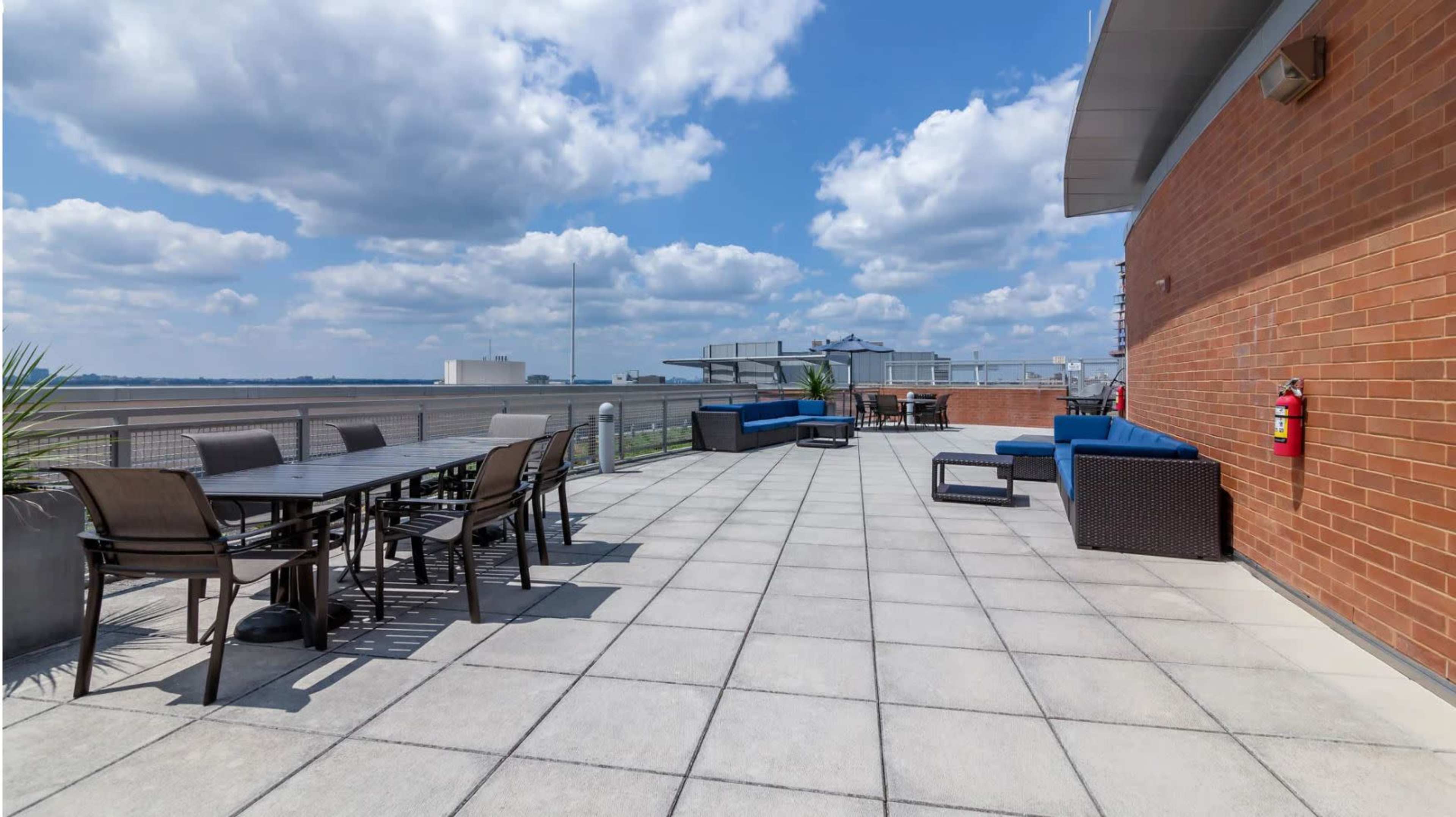 A spacious rooftop terrace with tables, chairs, and lounge seating against a backdrop of partly cloudy skies.