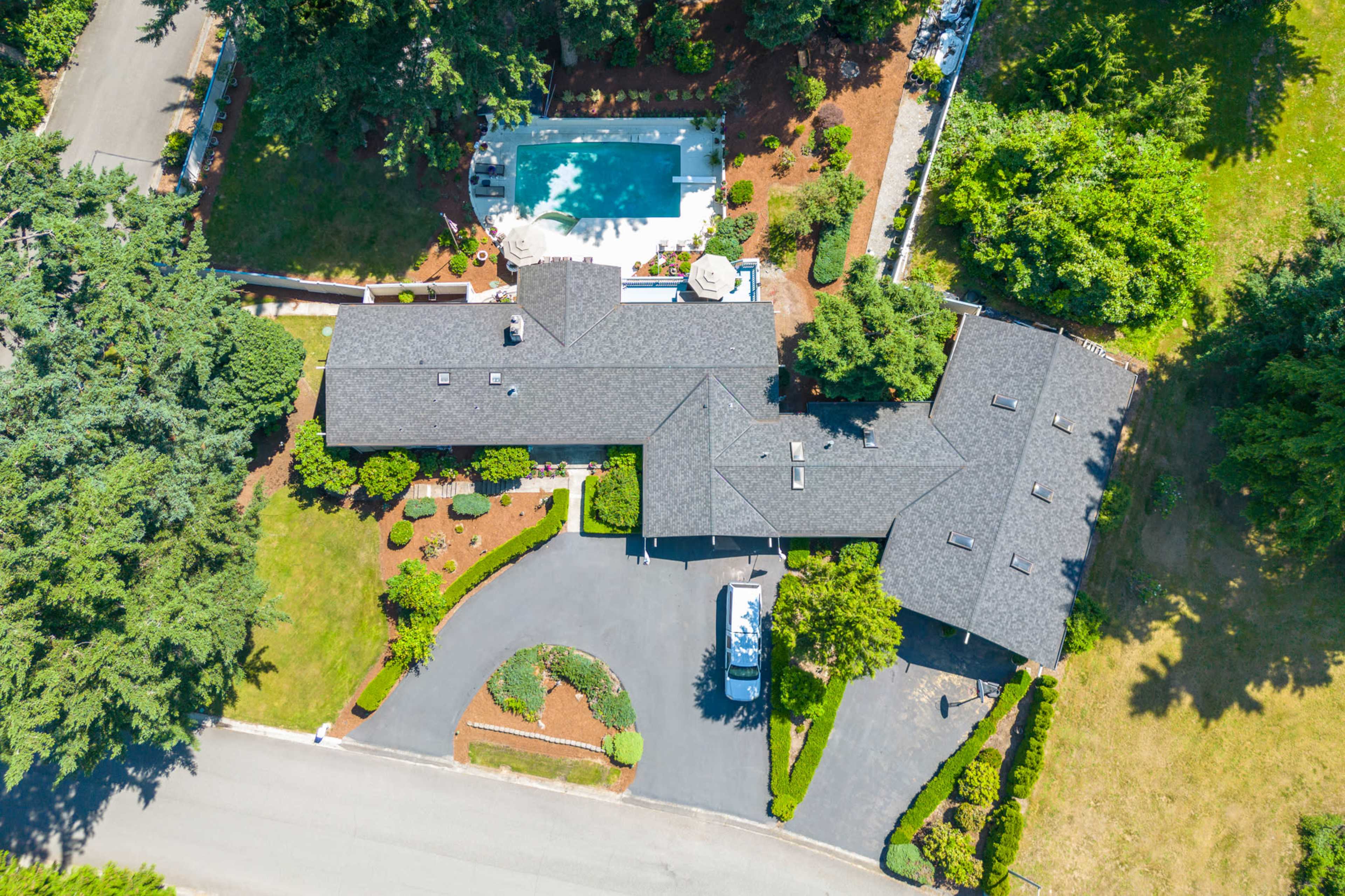 An aerial view of a large residence with a swimming pool, surrounded by greenery and a driveway leading off a road.
