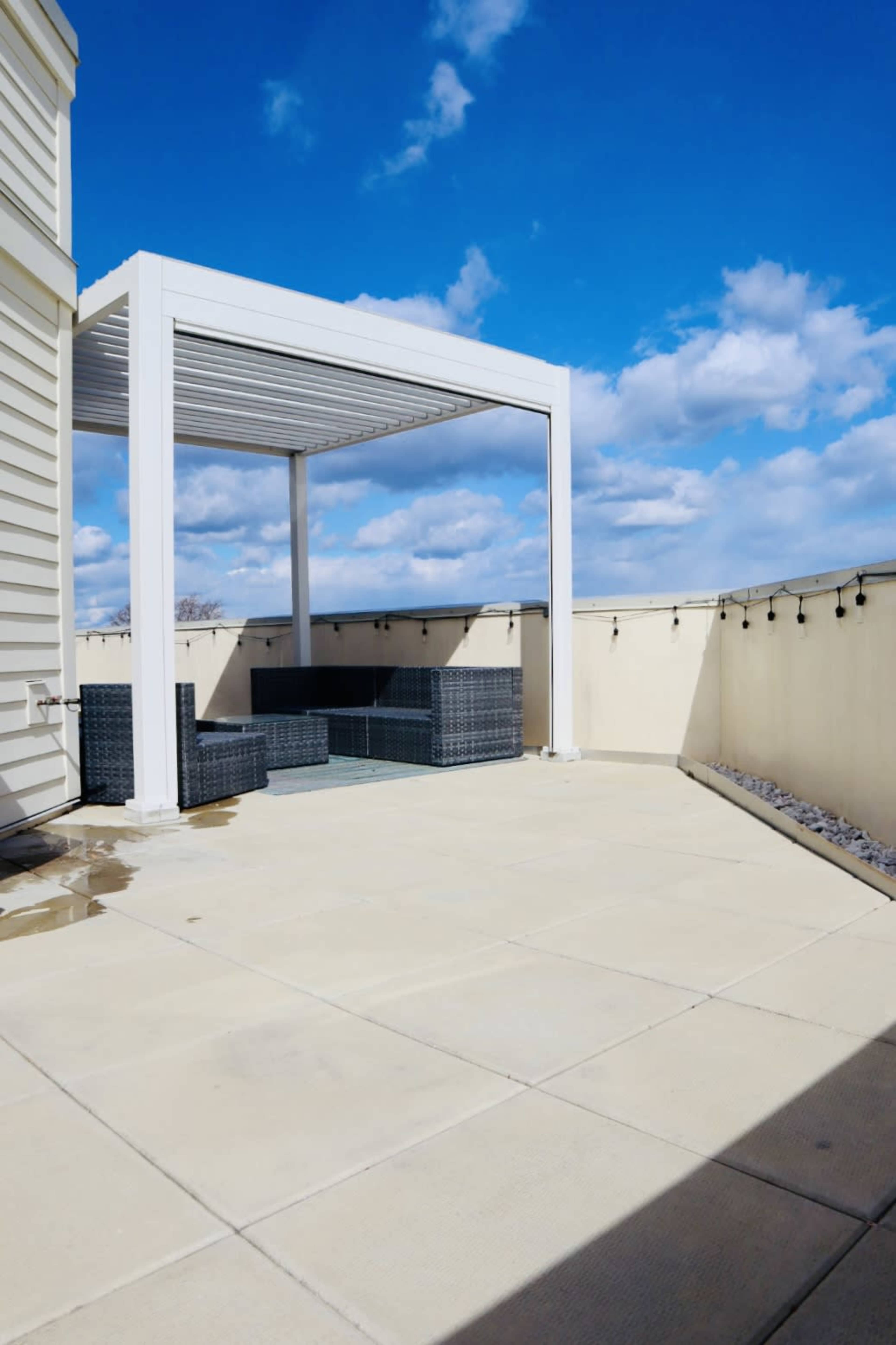 A rooftop patio with a pergola and outdoor seating area under a blue sky with clouds.