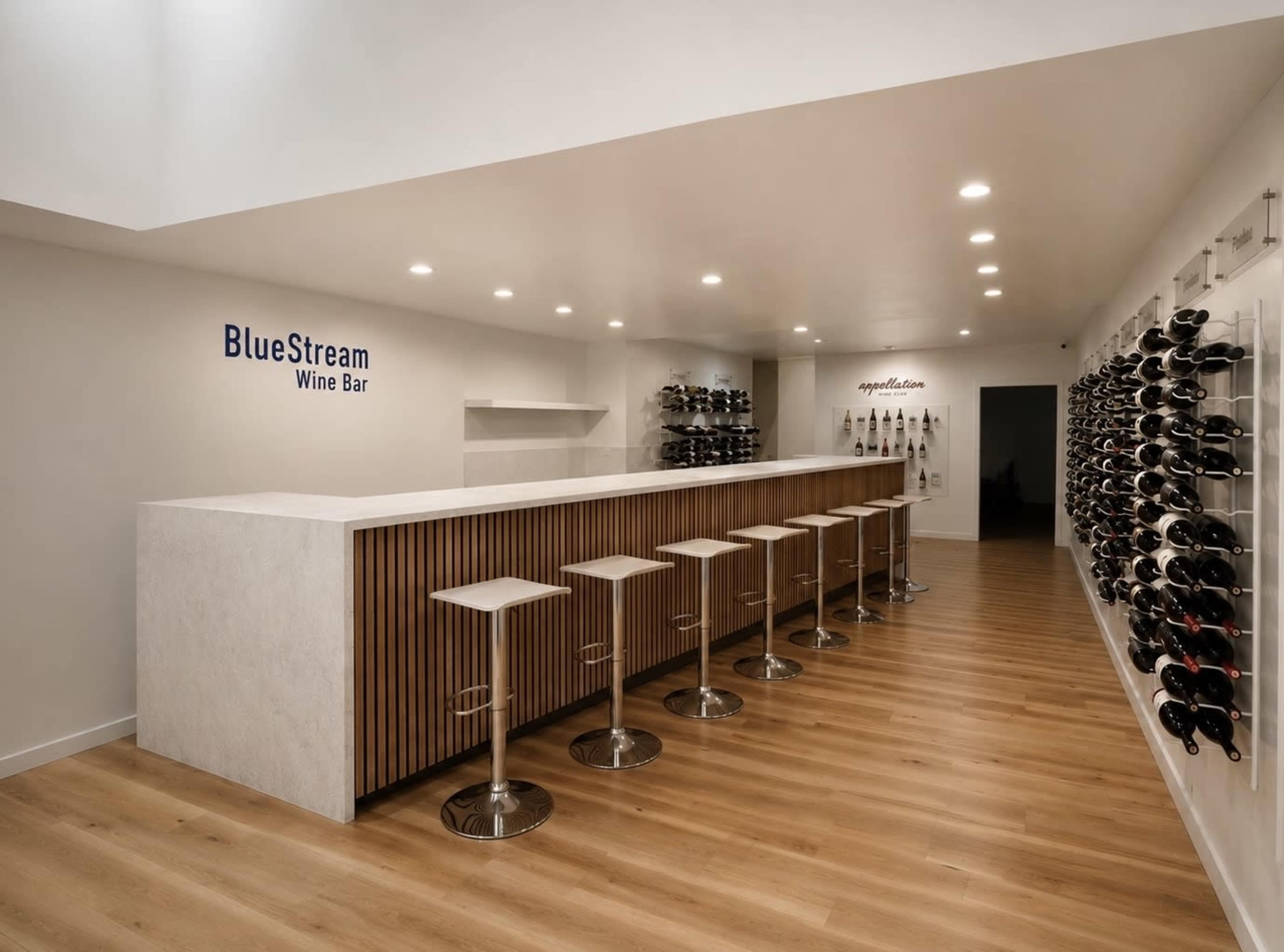 The image shows a modern wine bar with a long counter, high stools, and wine racks lining the walls.