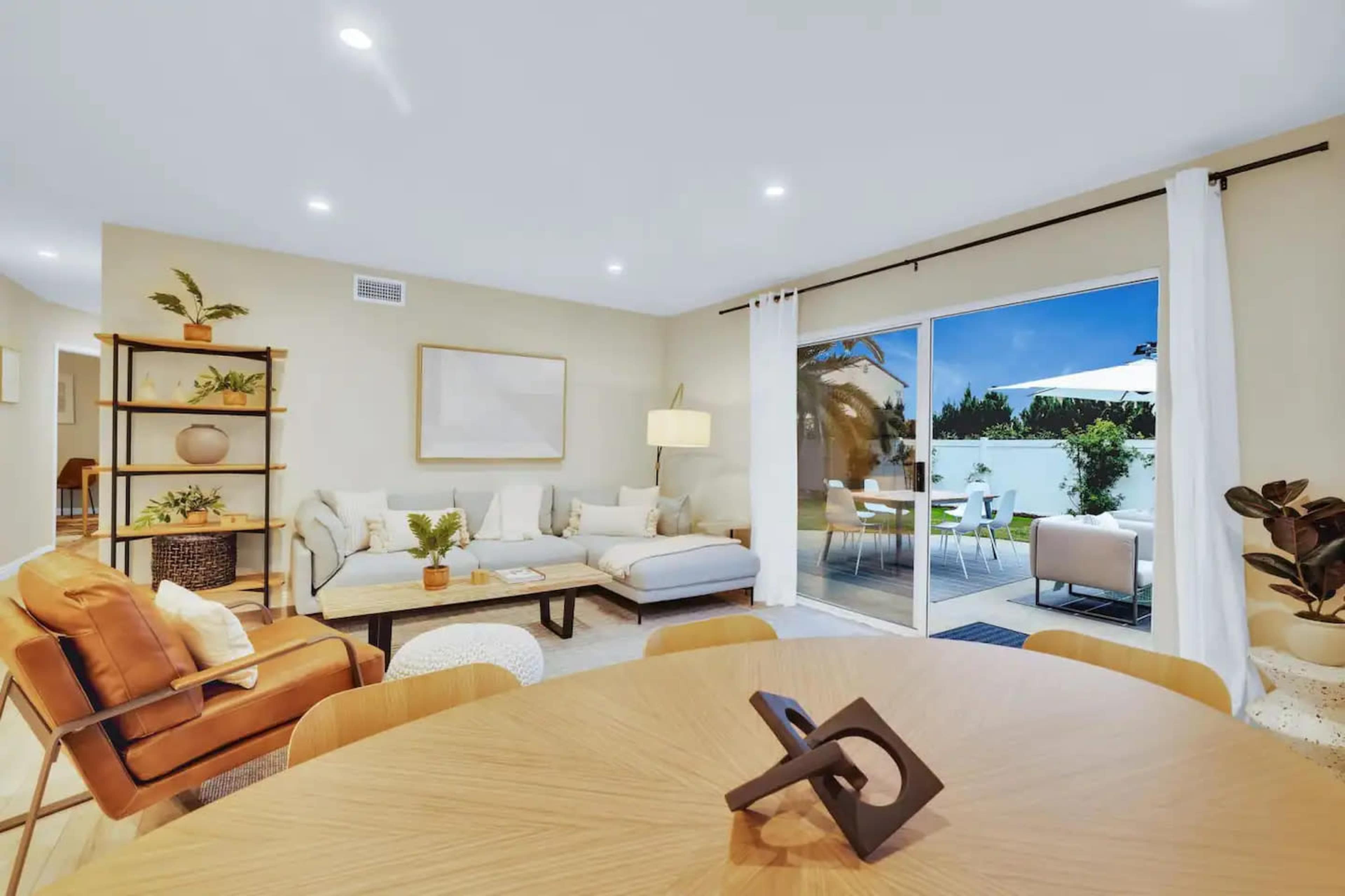 A modern living room features a sectional sofa, a round dining table, and sliding glass doors that open to an outdoor patio.