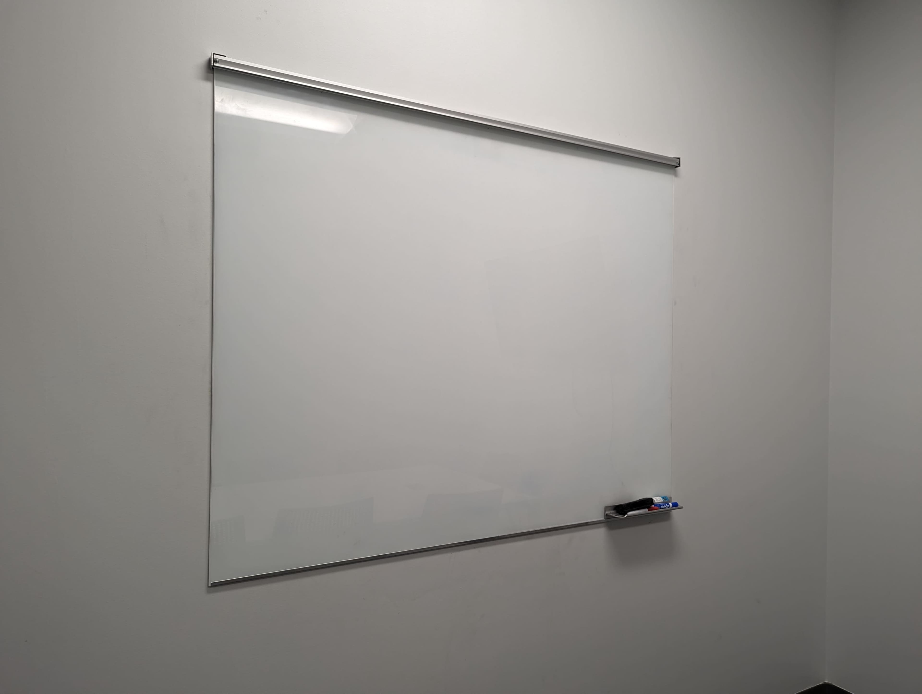 A blank whiteboard mounted on a plain wall, with a marker holder at the bottom.