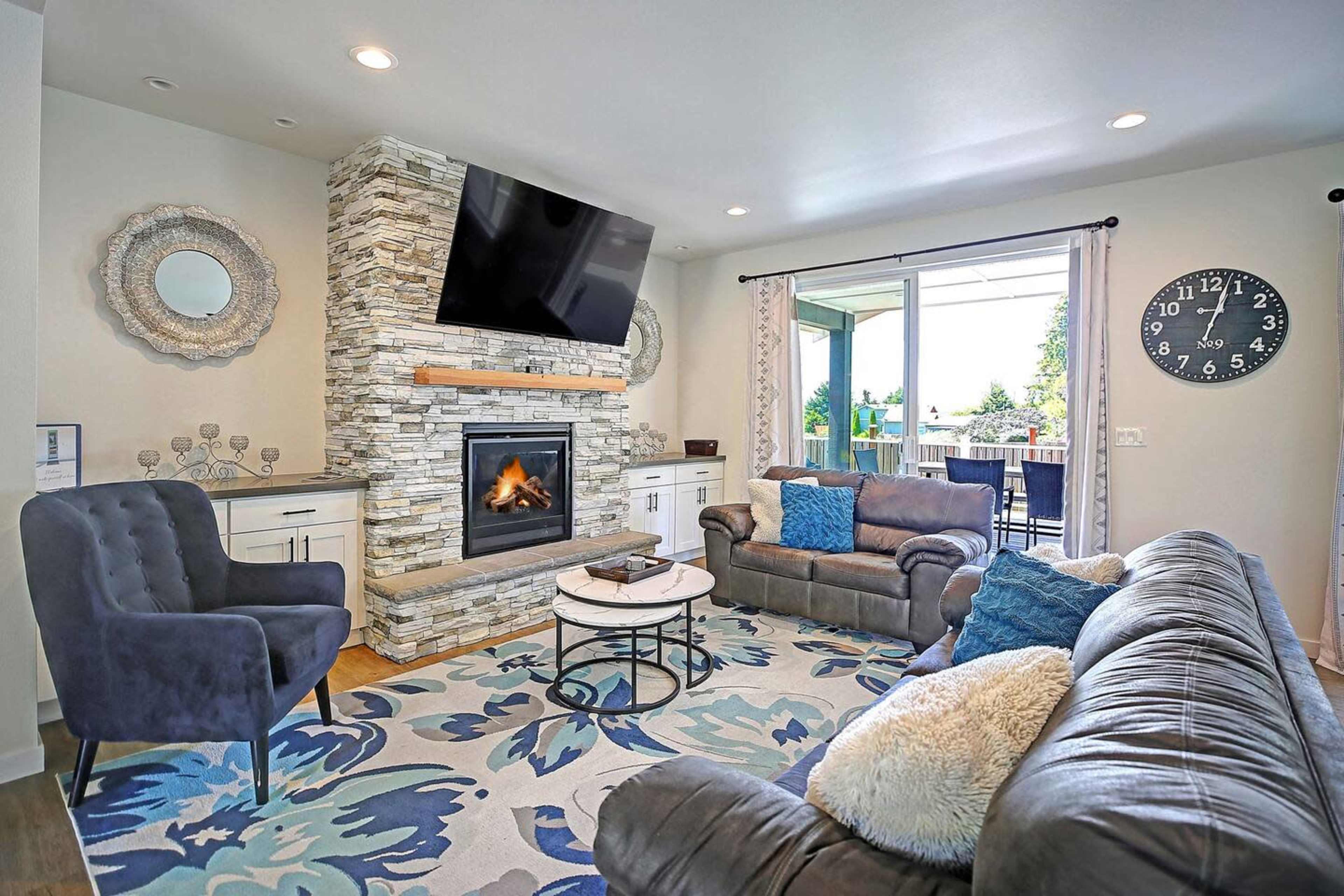 The living room features a stone fireplace with a mounted television, a circular coffee table, comfortable seating, and a patterned area rug.