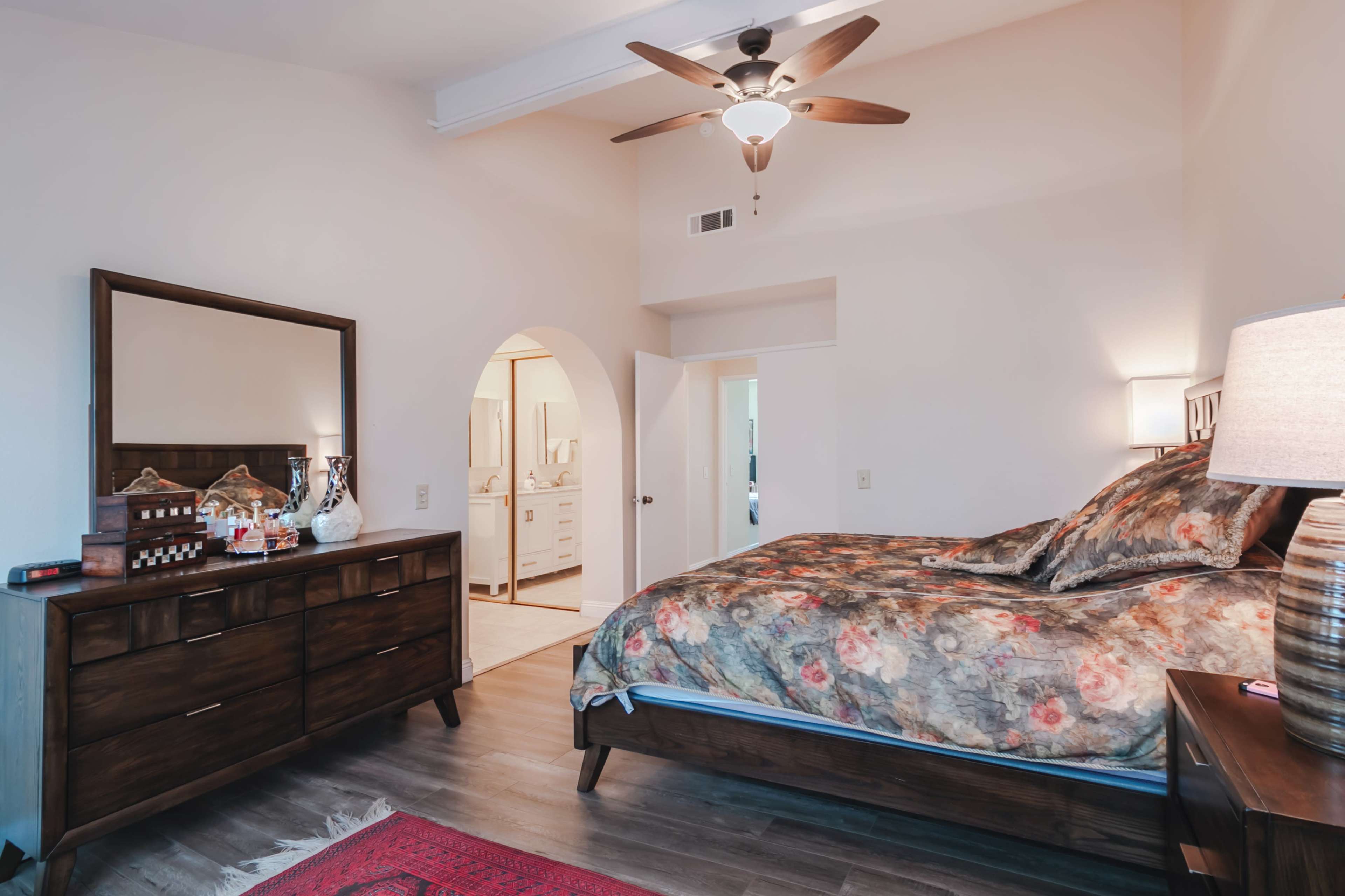 A spacious bedroom with a wooden bed, a dresser, and a mirror, featuring a bathroom entrance in the background.