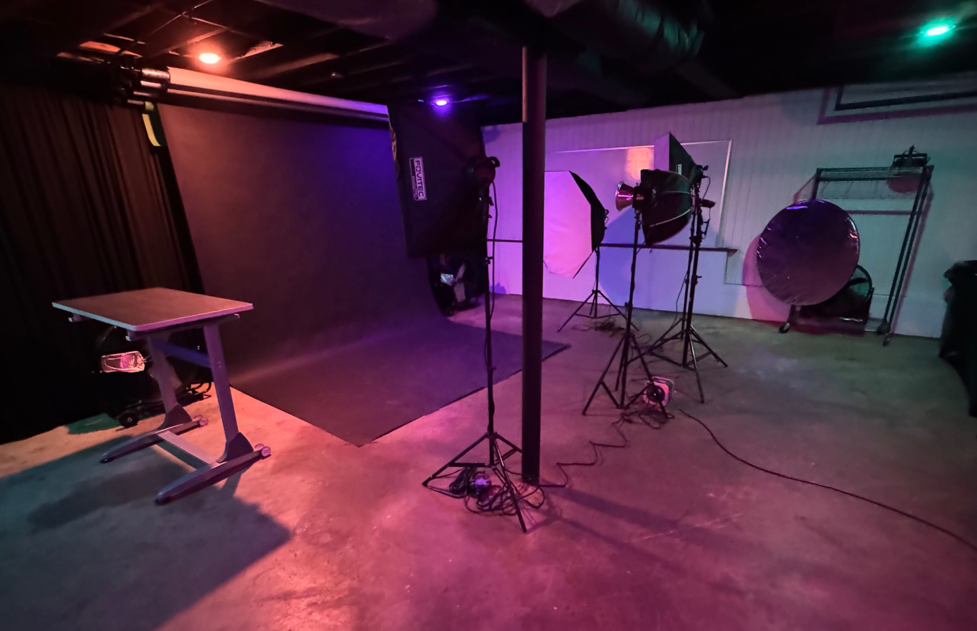 A photography studio setup with a backdrop, lighting equipment, and a table in a dimly lit basement space.