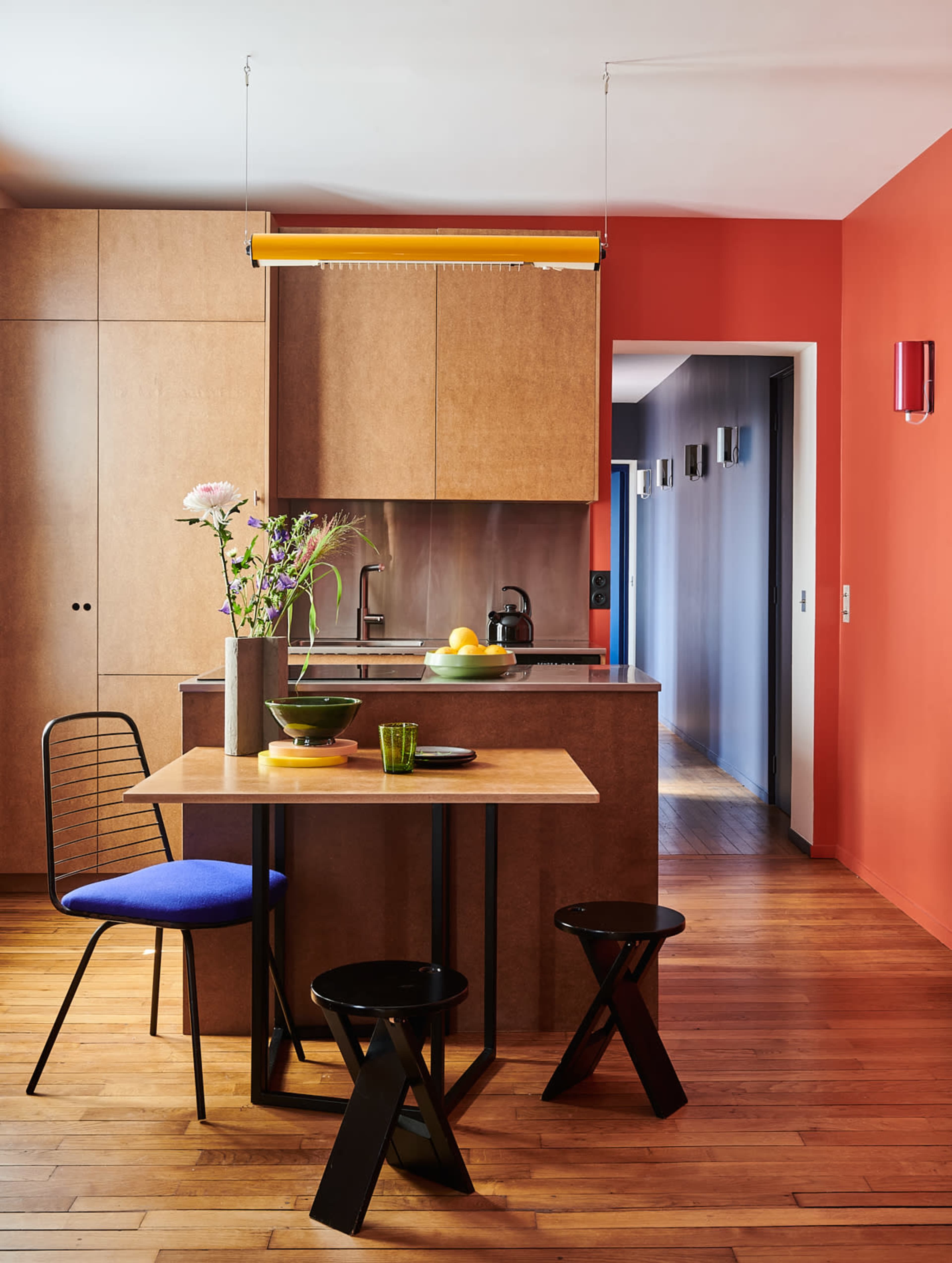 A modern kitchen features wooden cabinetry, a small dining table with black stools, and colorful accents on the walls.