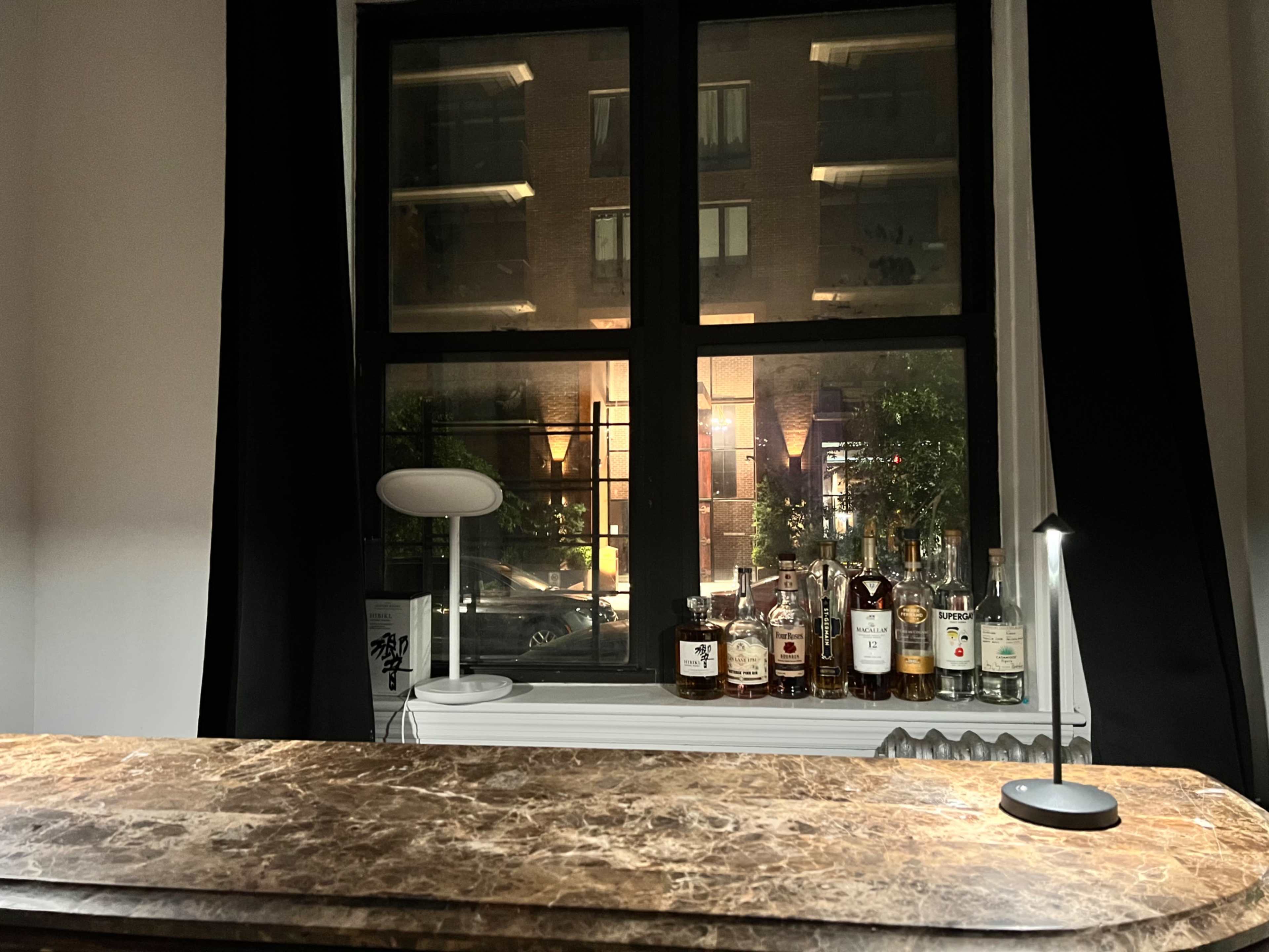 A bar counter with various bottles of liquor is visible in front of a large window overlooking a well-lit street.