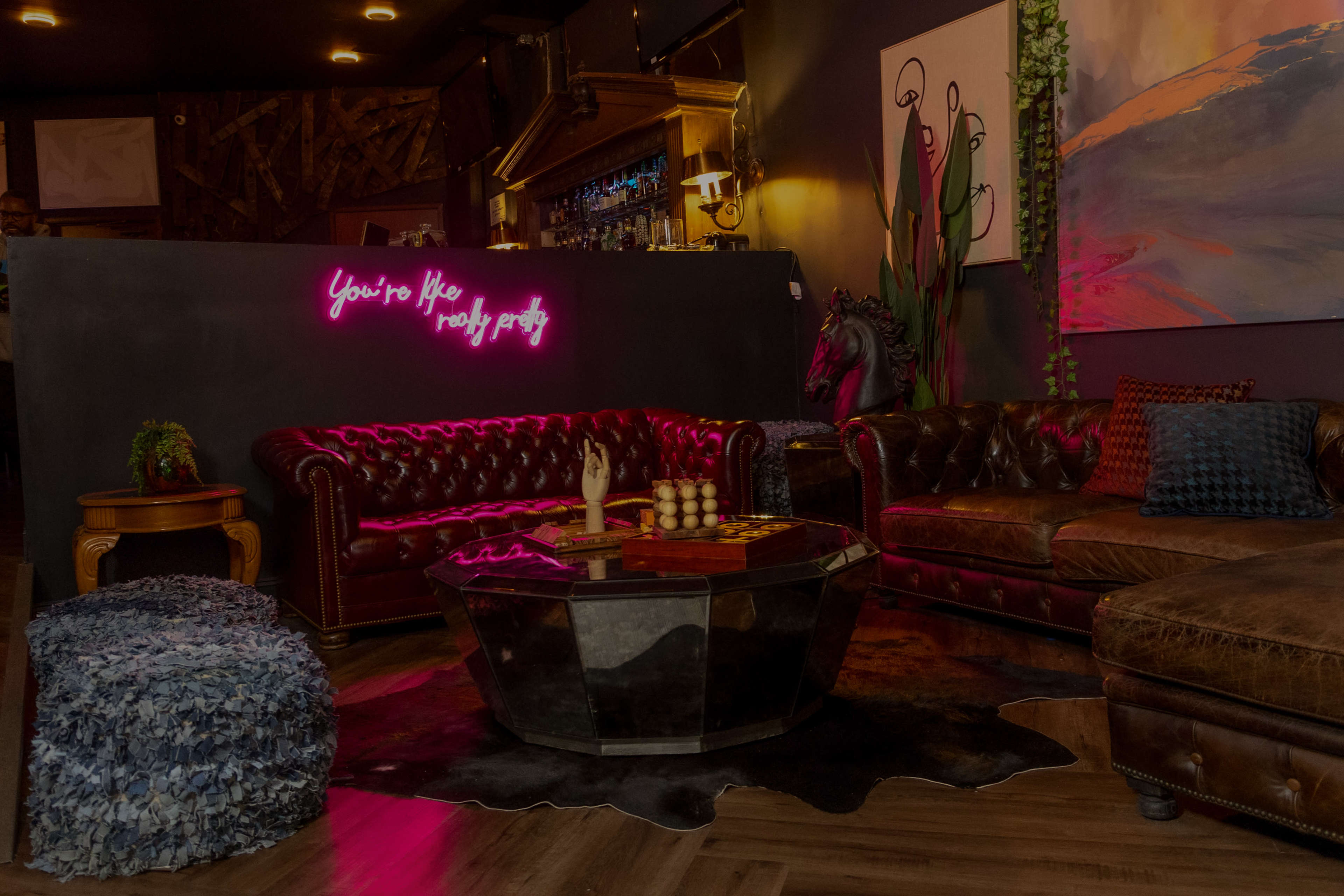 A cozy lounge area features a leather sofa, a wooden coffee table, and neon lighting on the wall.