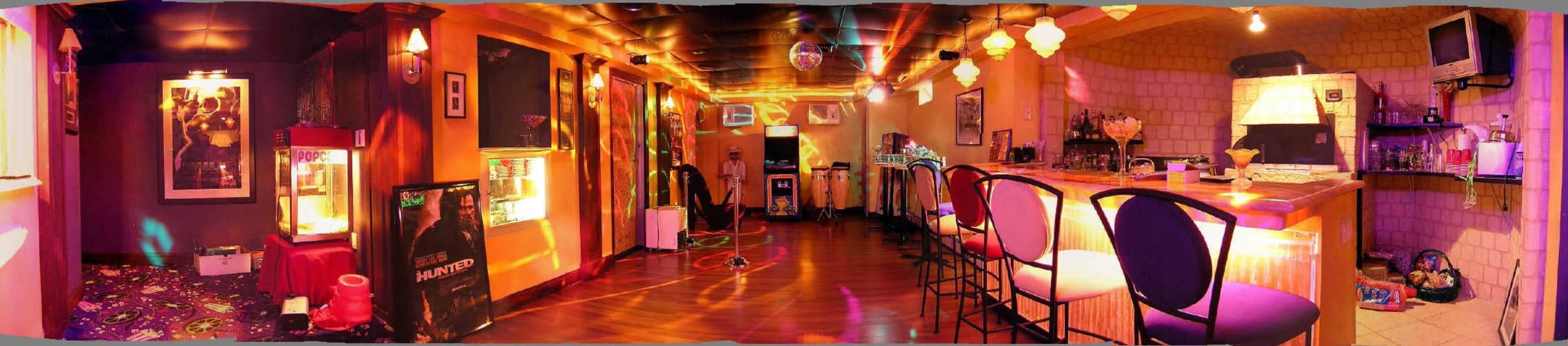 A brightly lit bar area with a long counter, colorful walls, and various decorations including a disco ball and arcade games.
