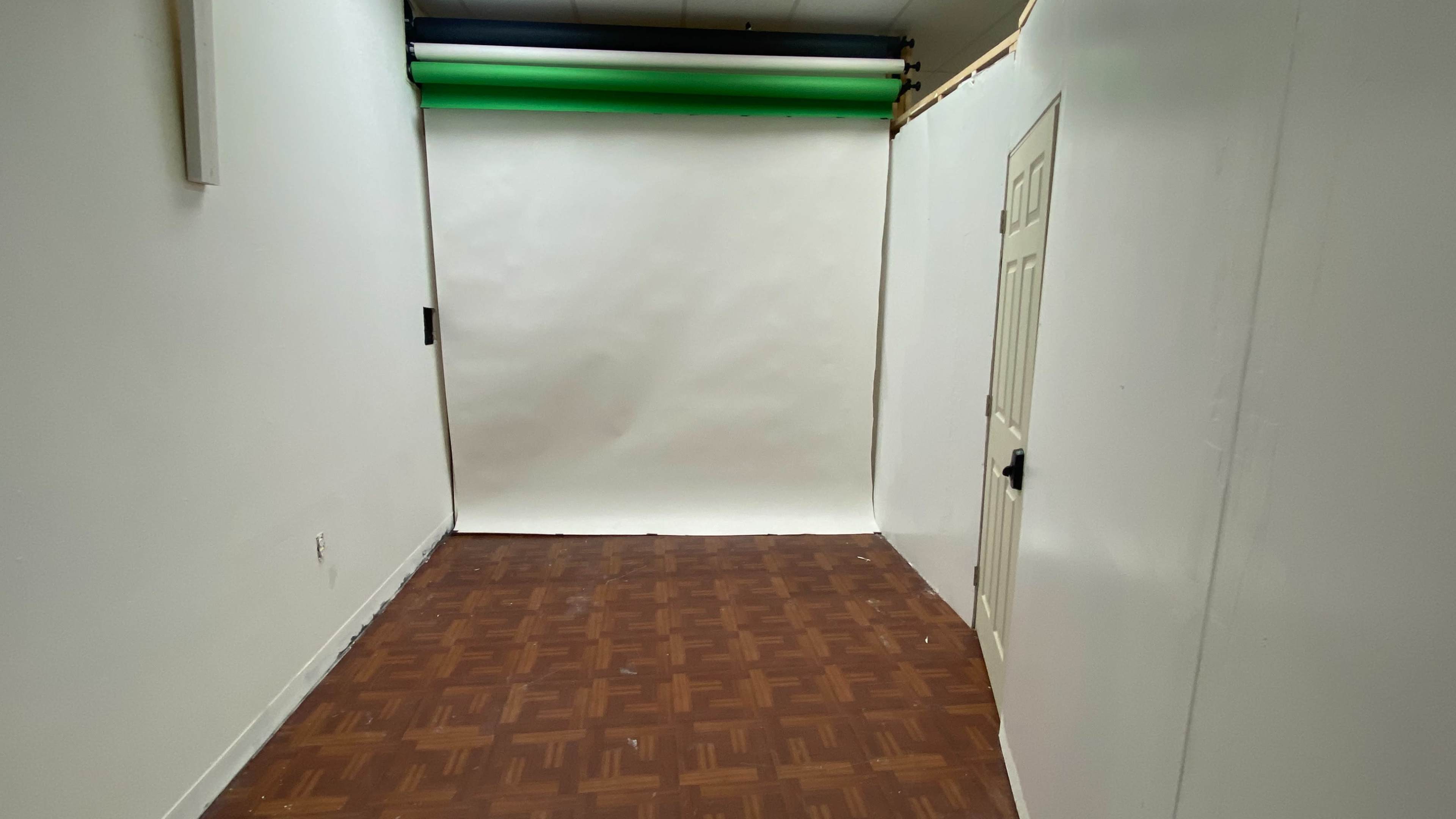 A vacant room with a parquet floor, a closed door, and a seamless background set up at one end.