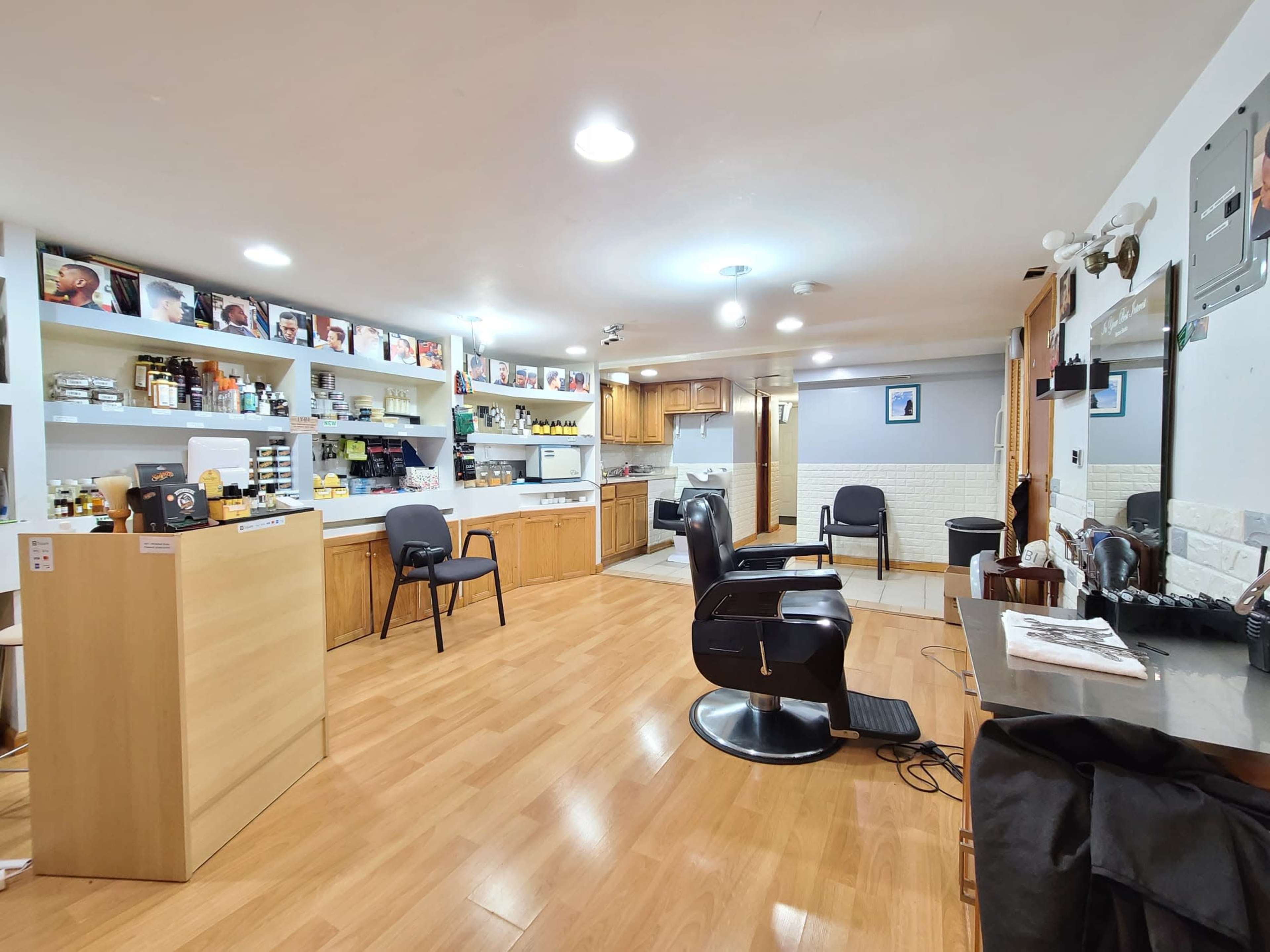 The image shows an interior of a salon with several styling chairs, a reception area, and shelves stocked with products.