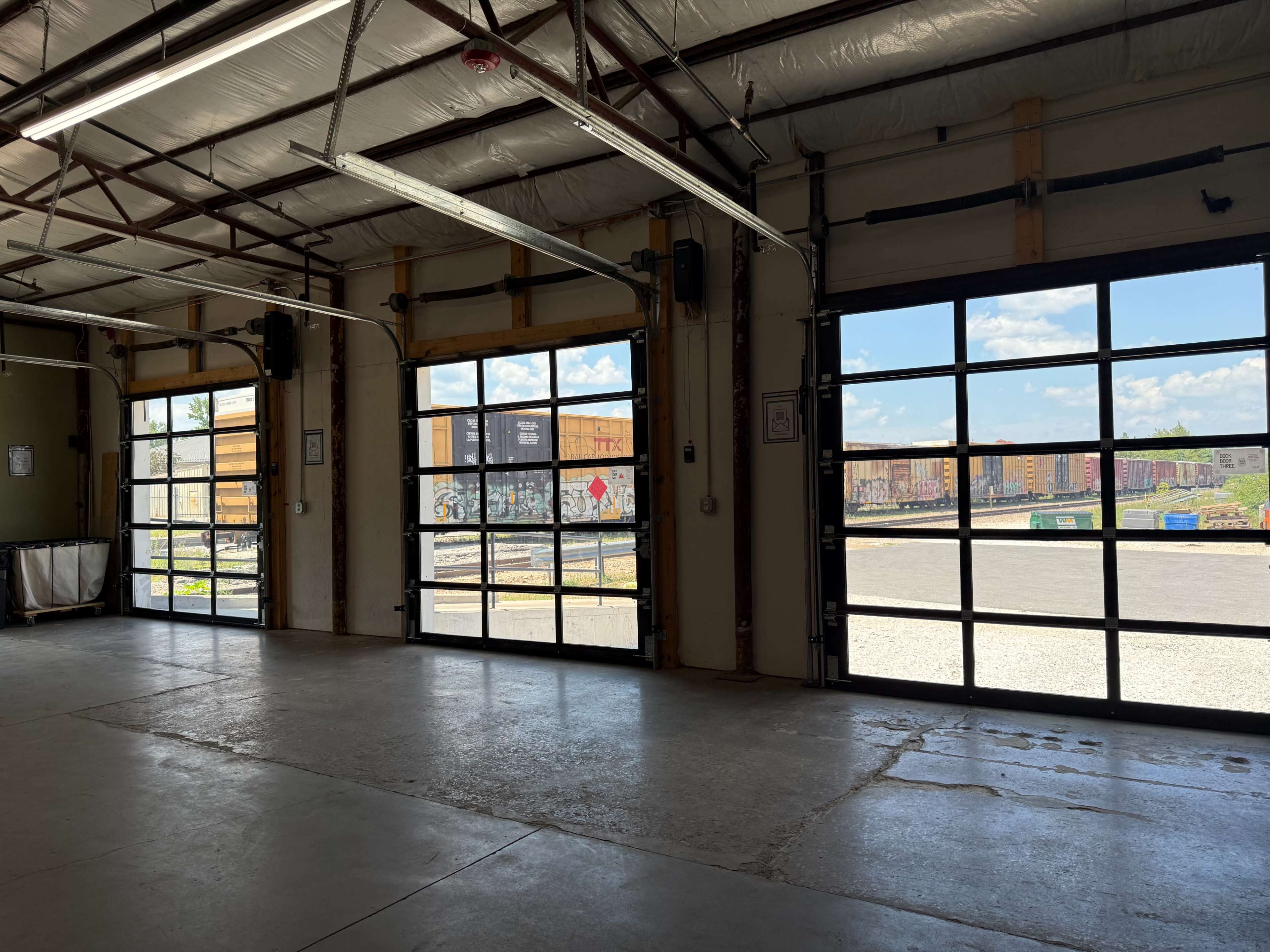 The image shows an industrial garage interior with large open doors revealing a view of freight train cars outside.