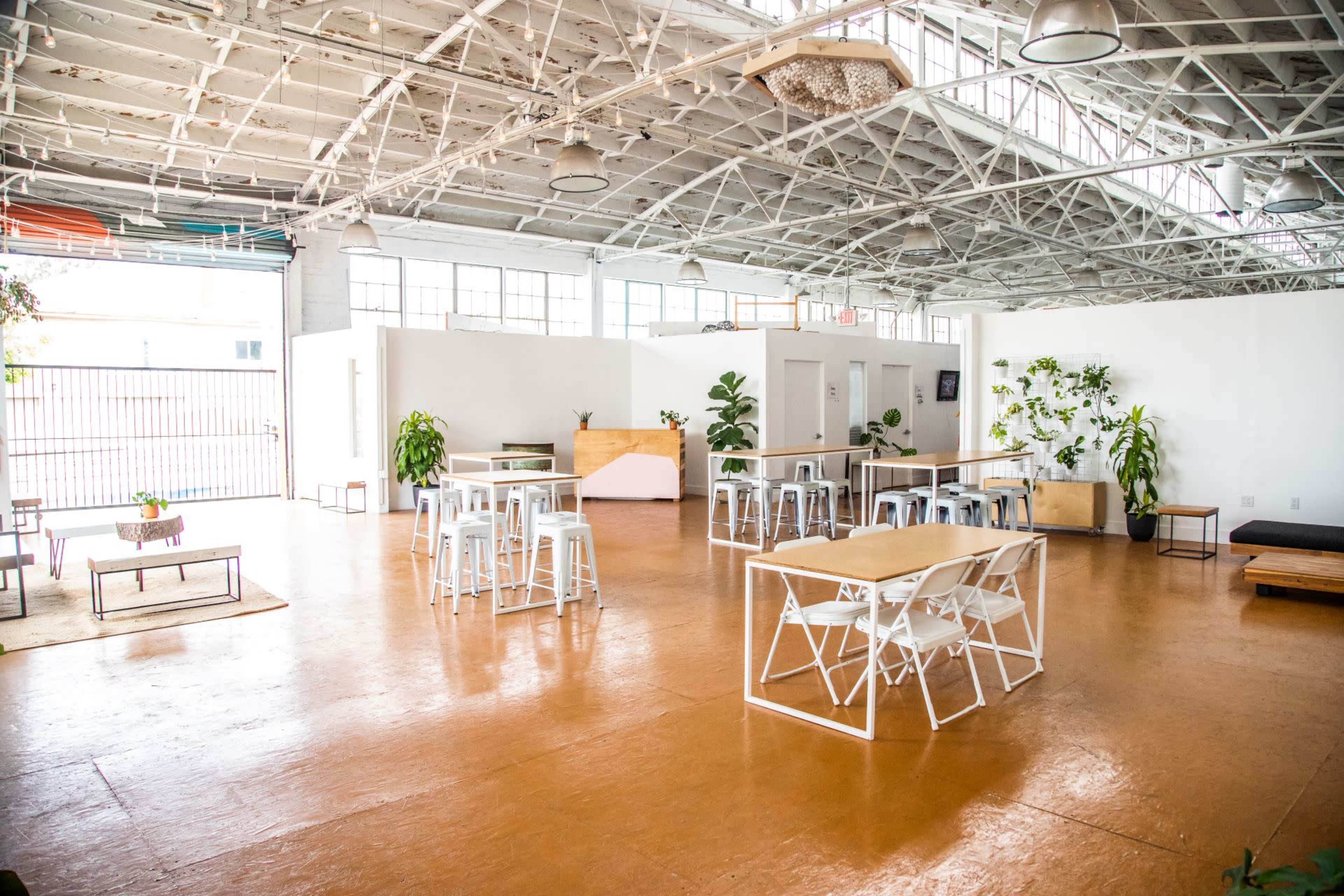 A spacious, well-lit indoor area with wooden floors, several tables and chairs, and a few plants placed around.