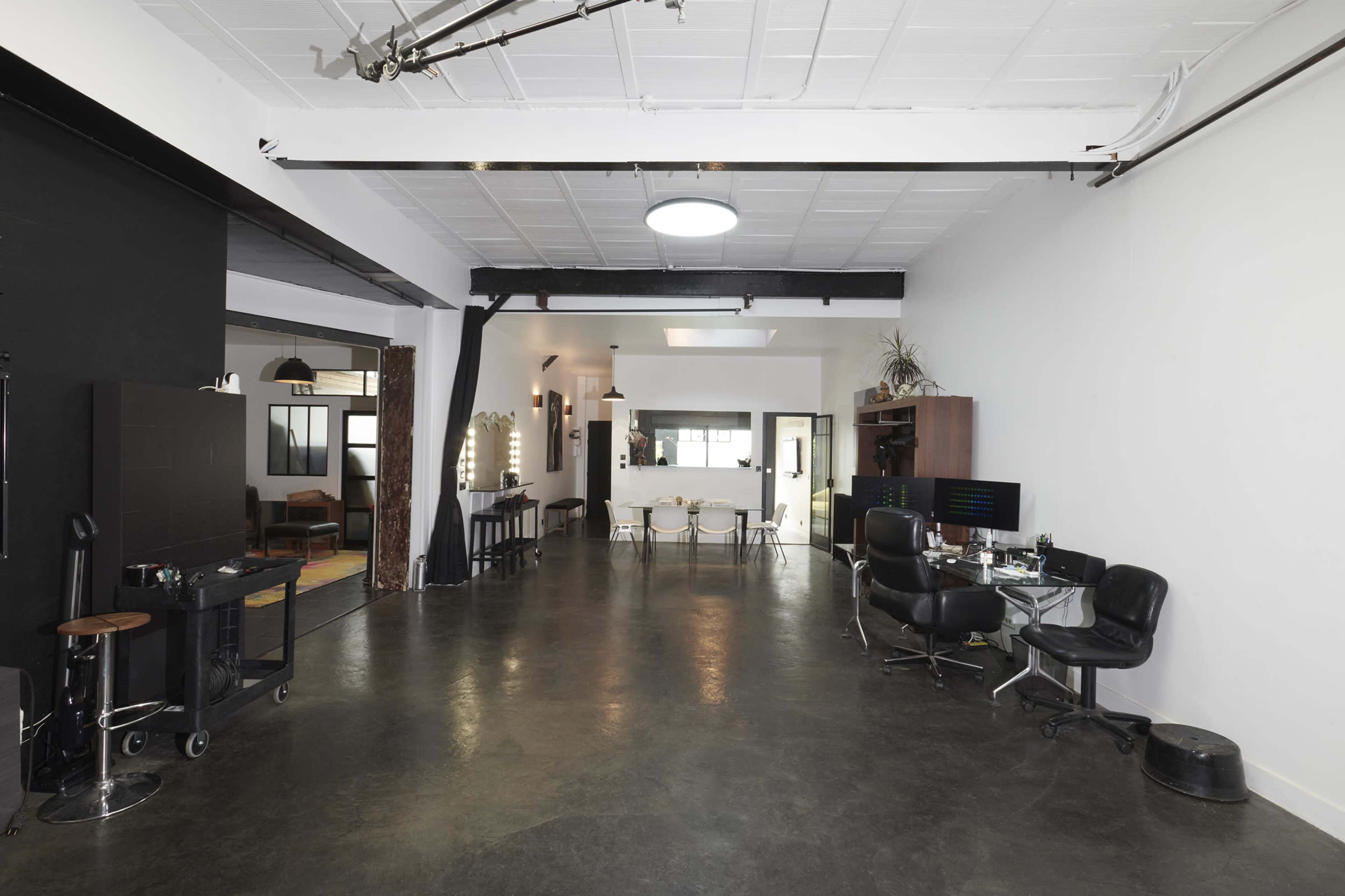 A spacious, modern studio with a polished concrete floor, black and white walls, and various furniture arrangements, including styling chairs and tables.