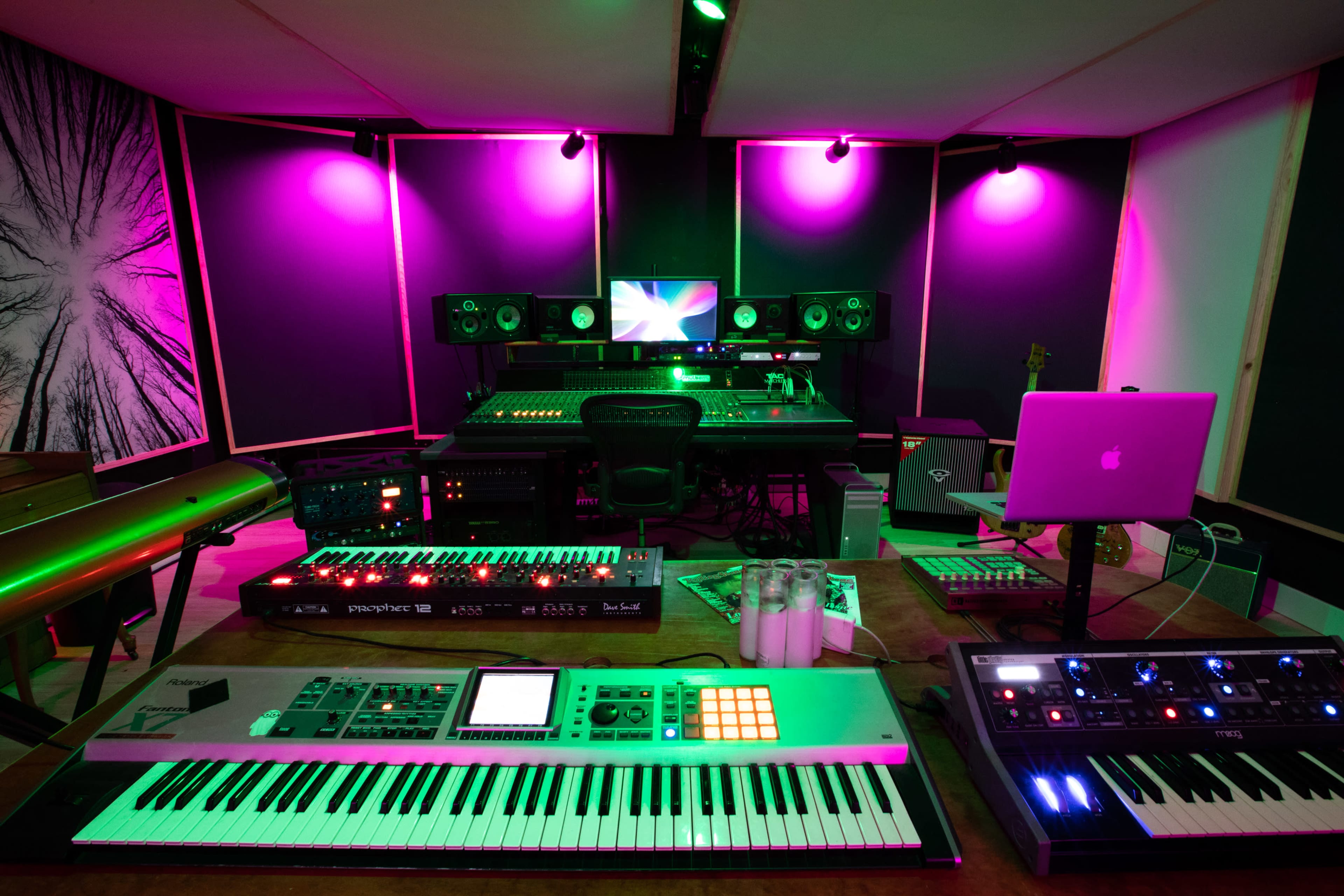 A music production studio features various synthesizers, keyboards, and speakers, illuminated by purple lights.