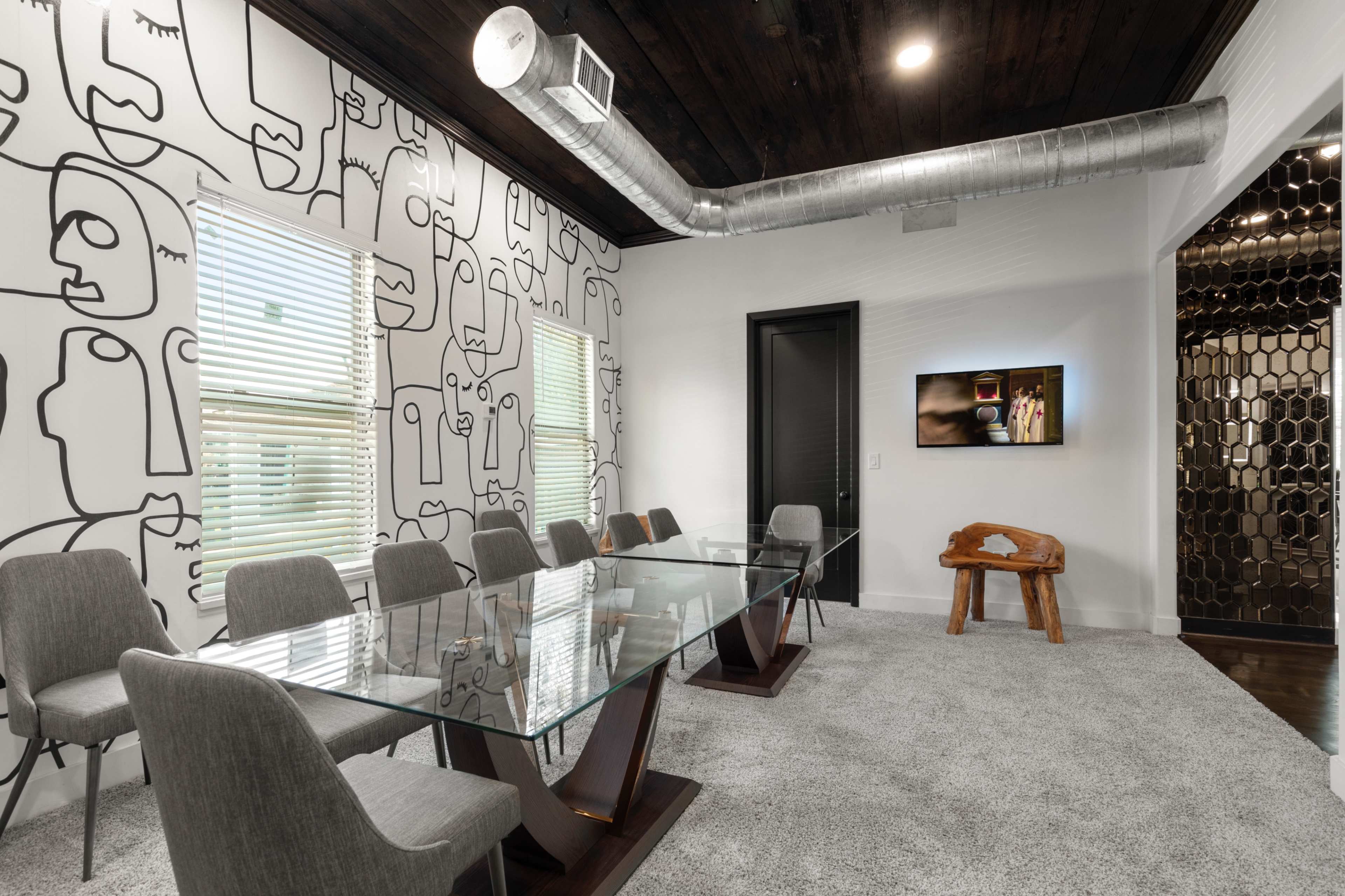 A modern conference room with a glass table, gray chairs, and a wall featuring abstract line art.