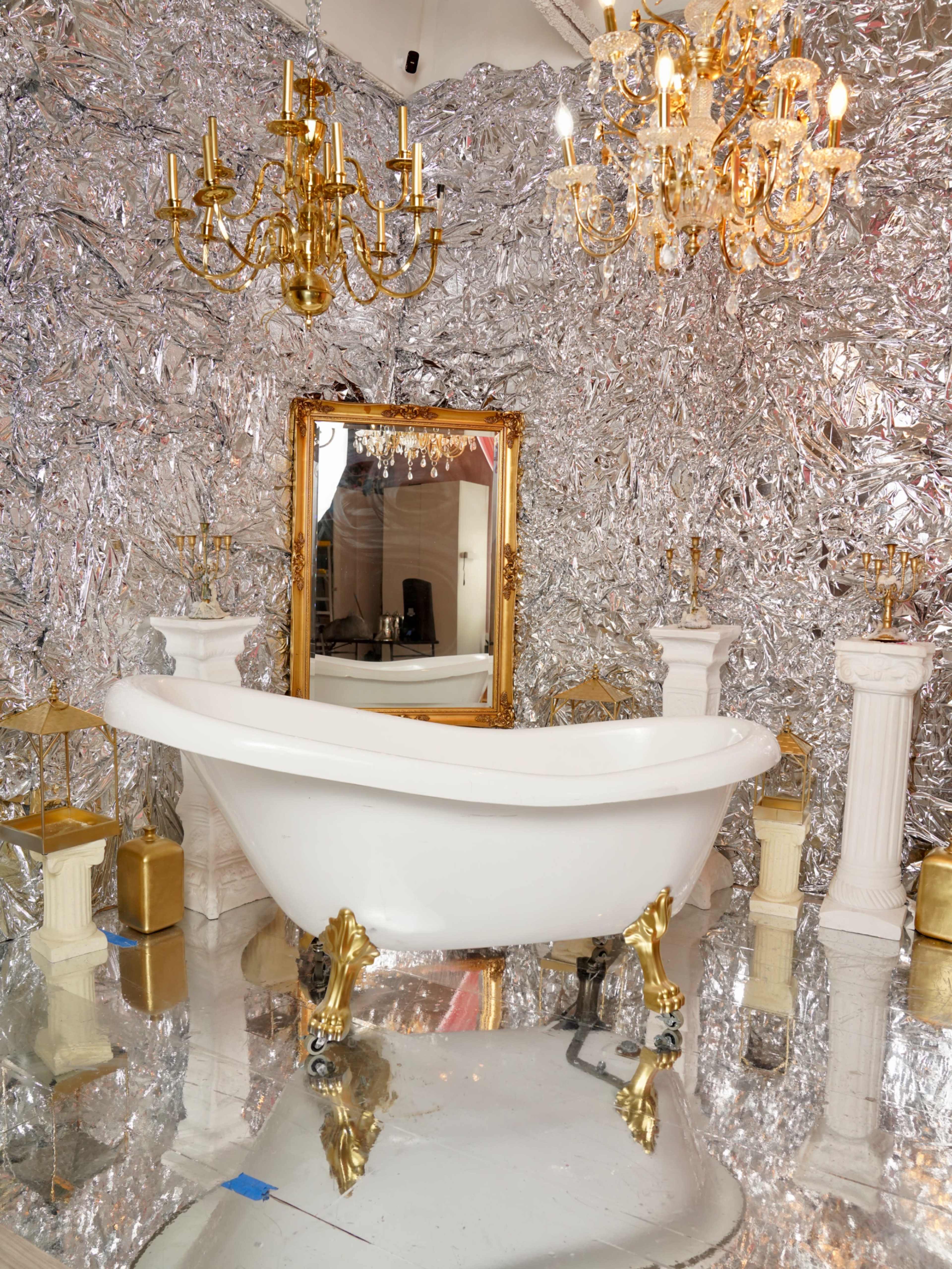 The image features a luxurious bathroom with a white vintage bathtub, gold accents, and walls covered in shiny silver foil.