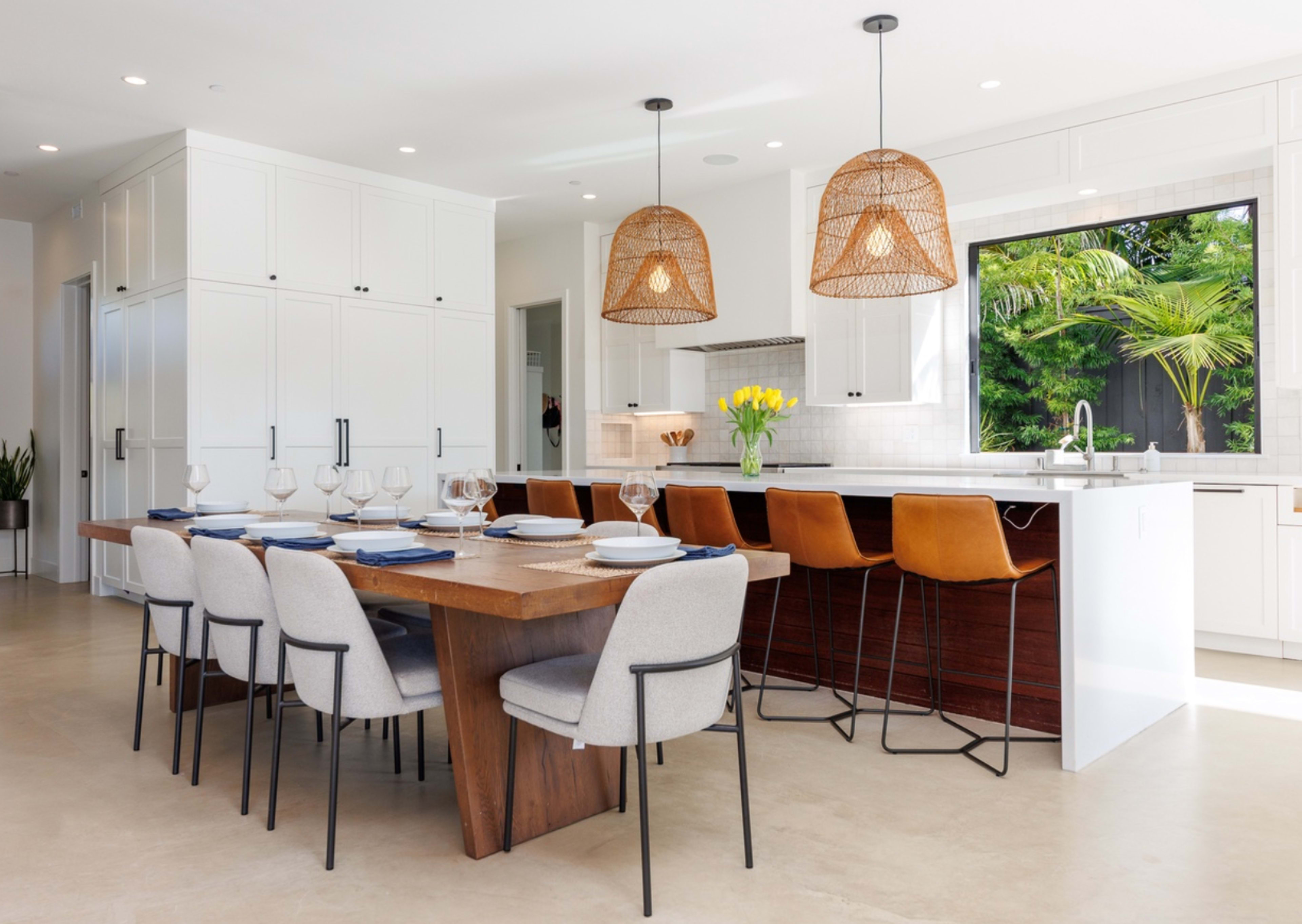 A modern kitchen features a wooden dining table set for six, with four chairs and a long kitchen island adorned with two pendant lights and bar seating for three.