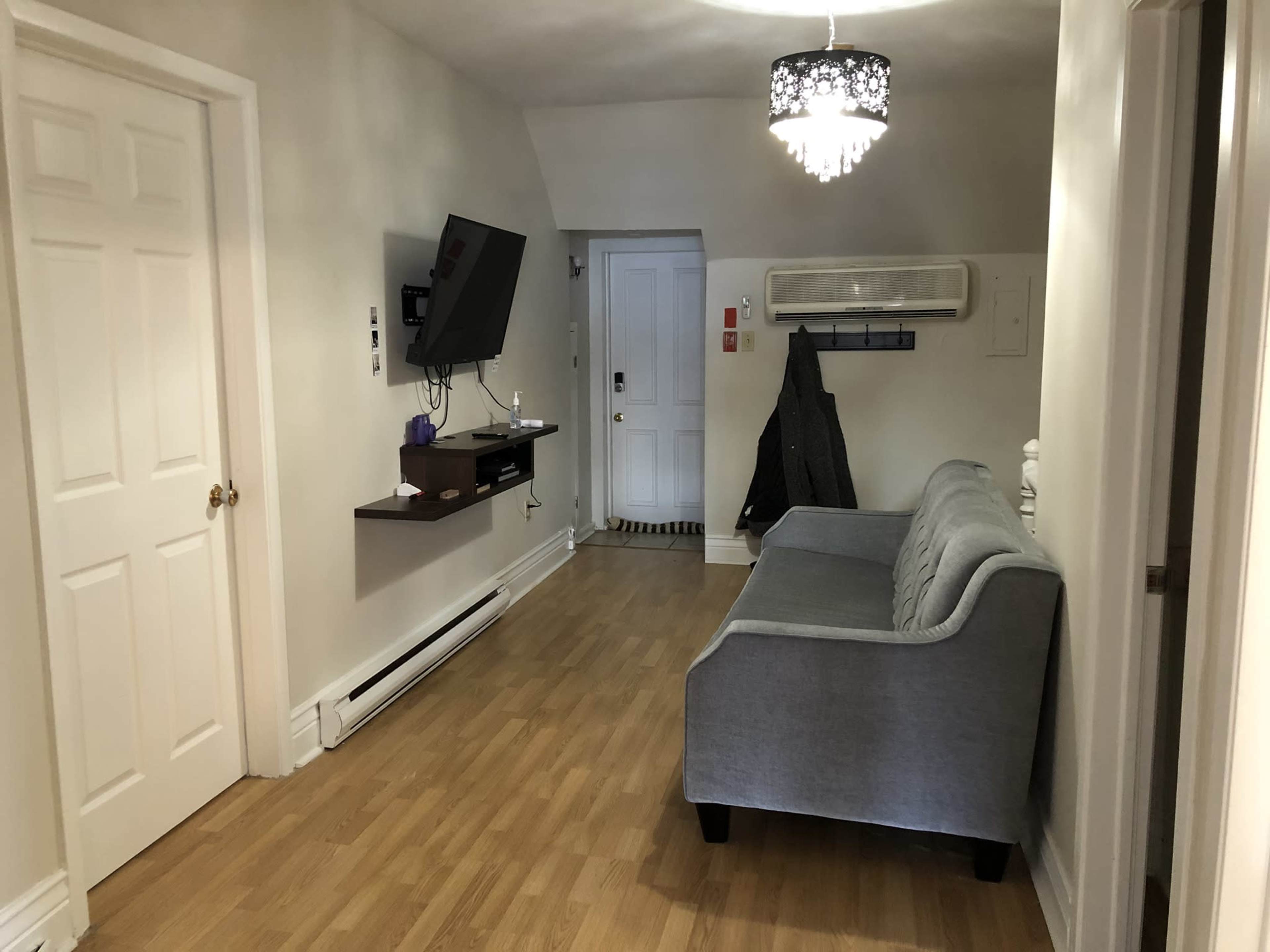 A simple living room with a gray couch, a wall-mounted television, and a door leading outside.