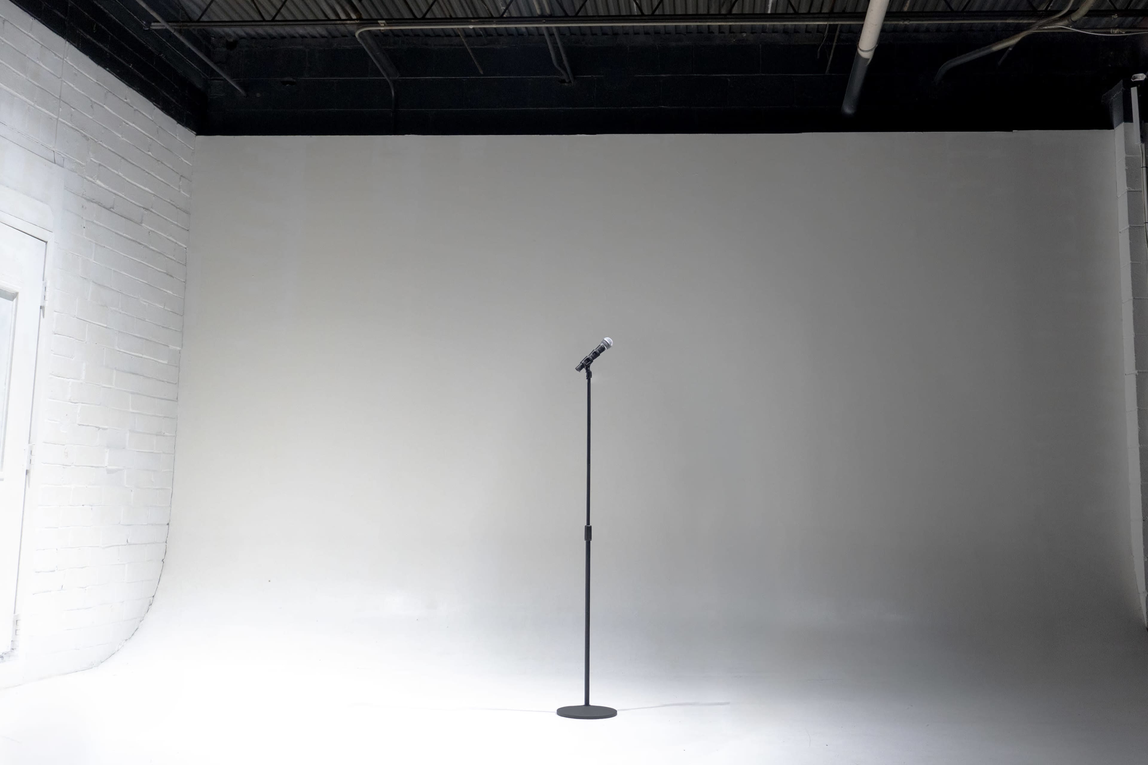 A microphone stand is positioned in the center of a simple, empty studio space with a white backdrop.