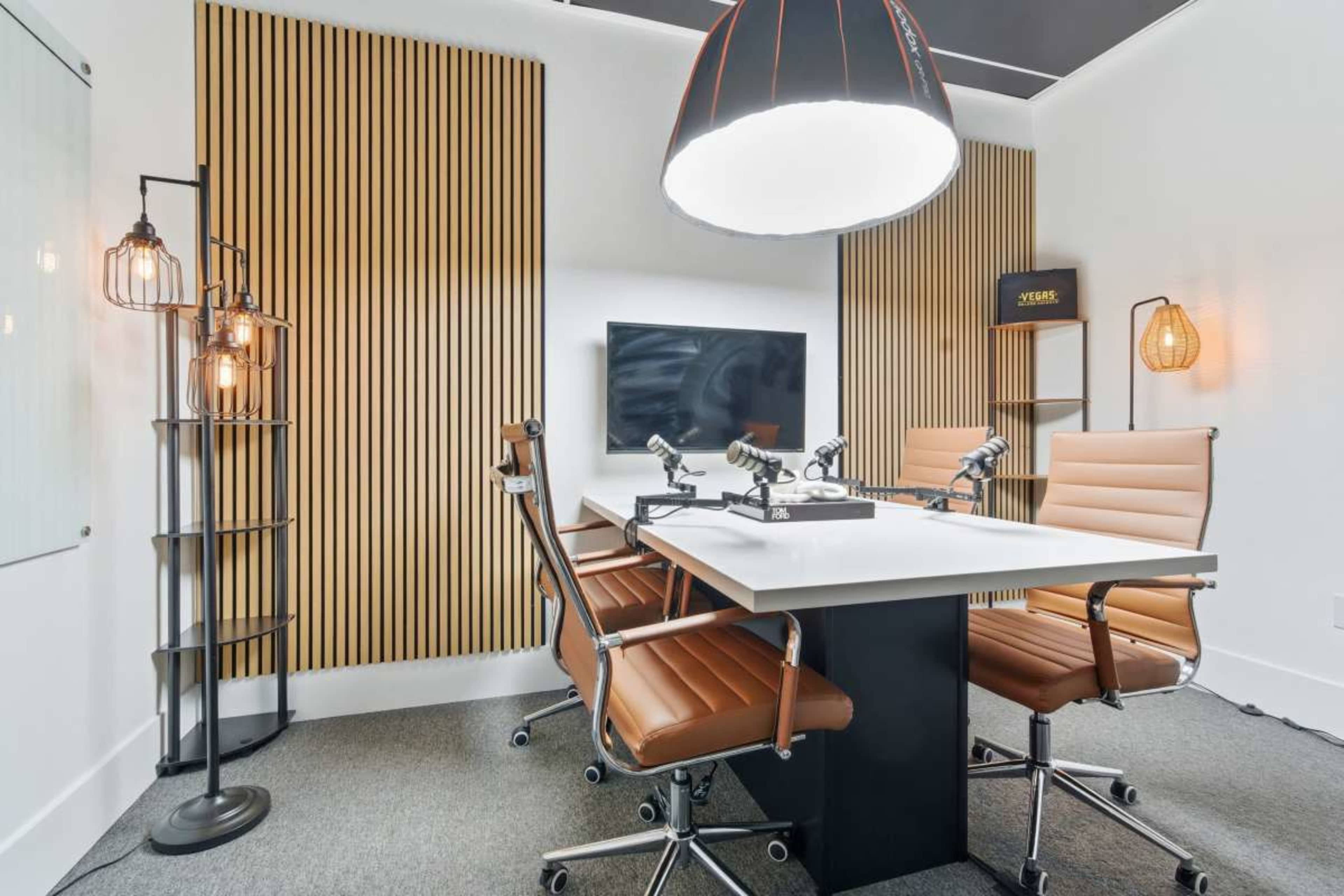 The image shows a modern conference room with a table surrounded by four leather chairs, a television on the wall, and stylish lighting fixtures.