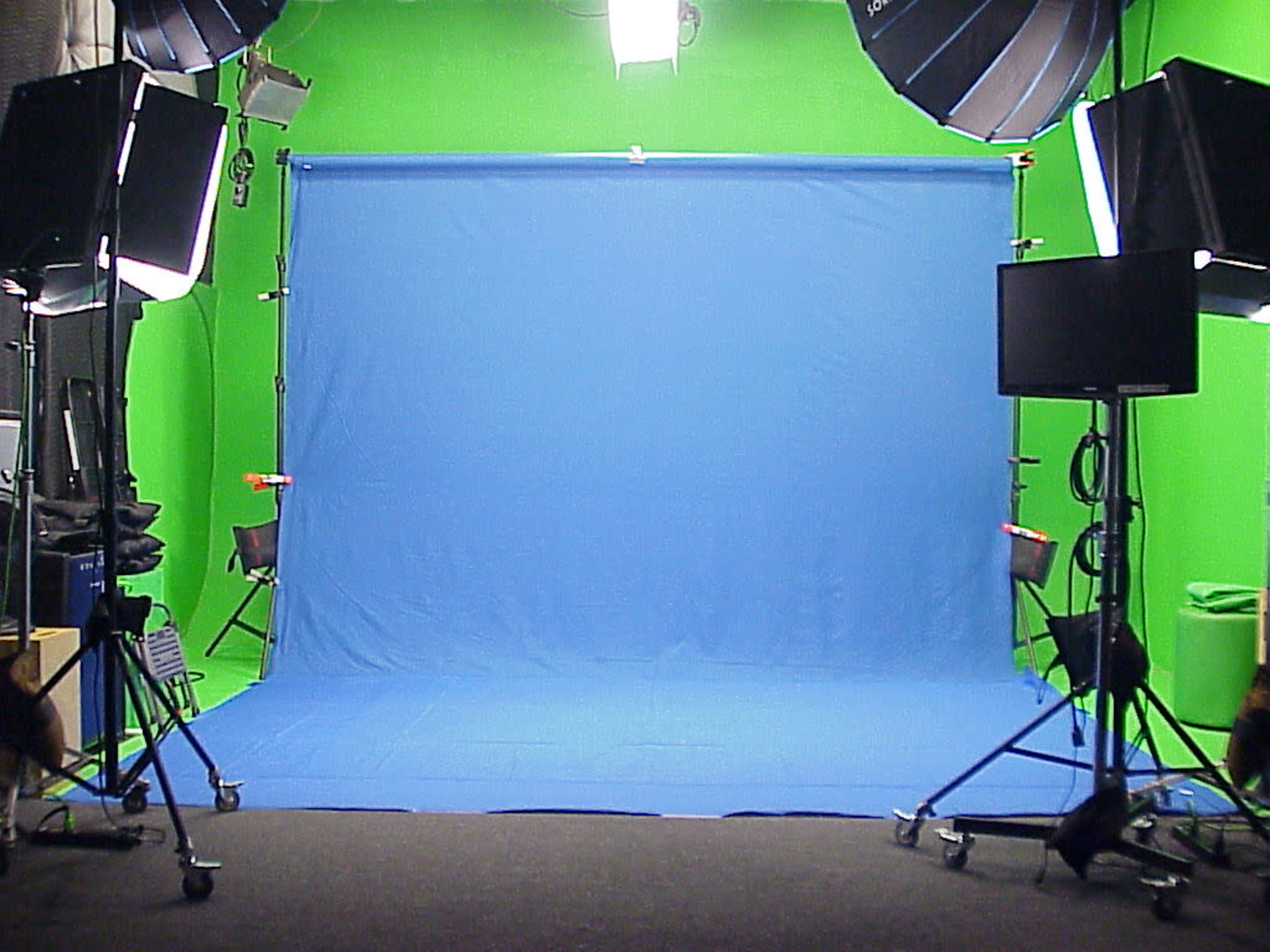 A photography studio featuring a blue backdrop with green moveable lighting setups on either side.
